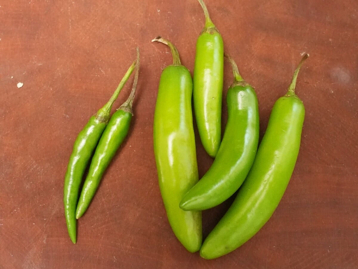 Thai chilies next to serrano chilies on a cutting board.