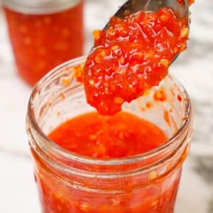 Cooked Sweet Thai Chili Sauce in a jar with a spoon.