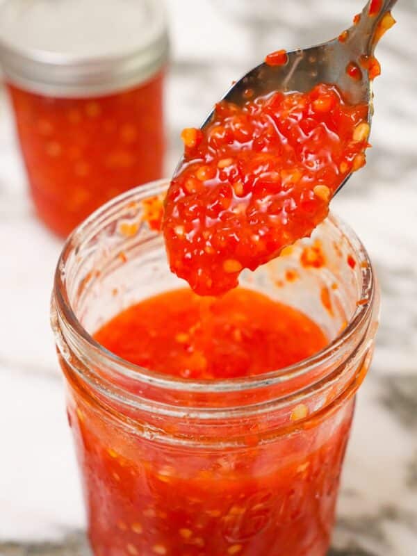 Cooked Sweet Thai Chili Sauce in a jar with a spoon.