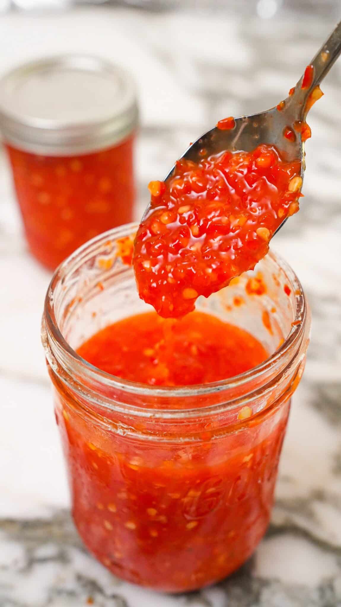 Cooked Sweet Thai Chili Sauce in a jar with a spoon.
