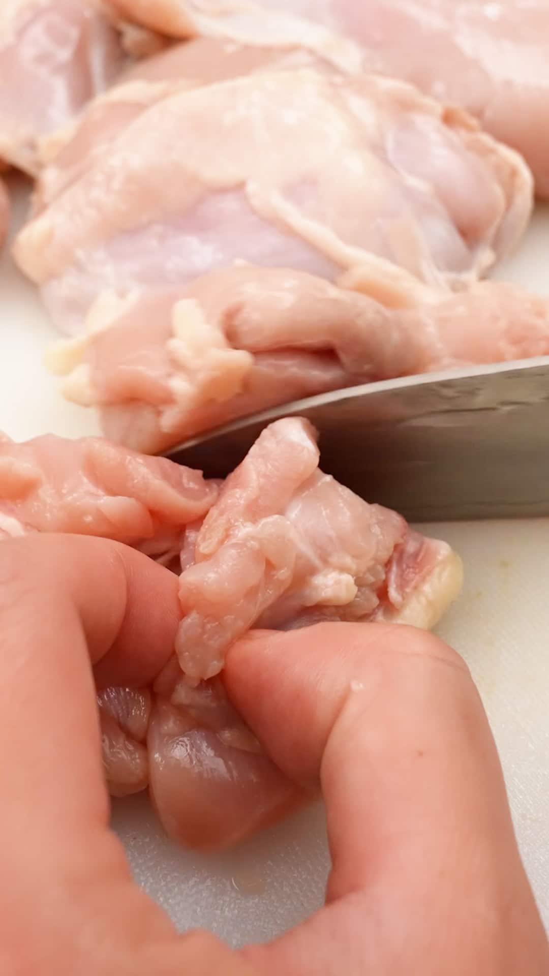 Slicing chicken thighs with a knife on a cutting board.