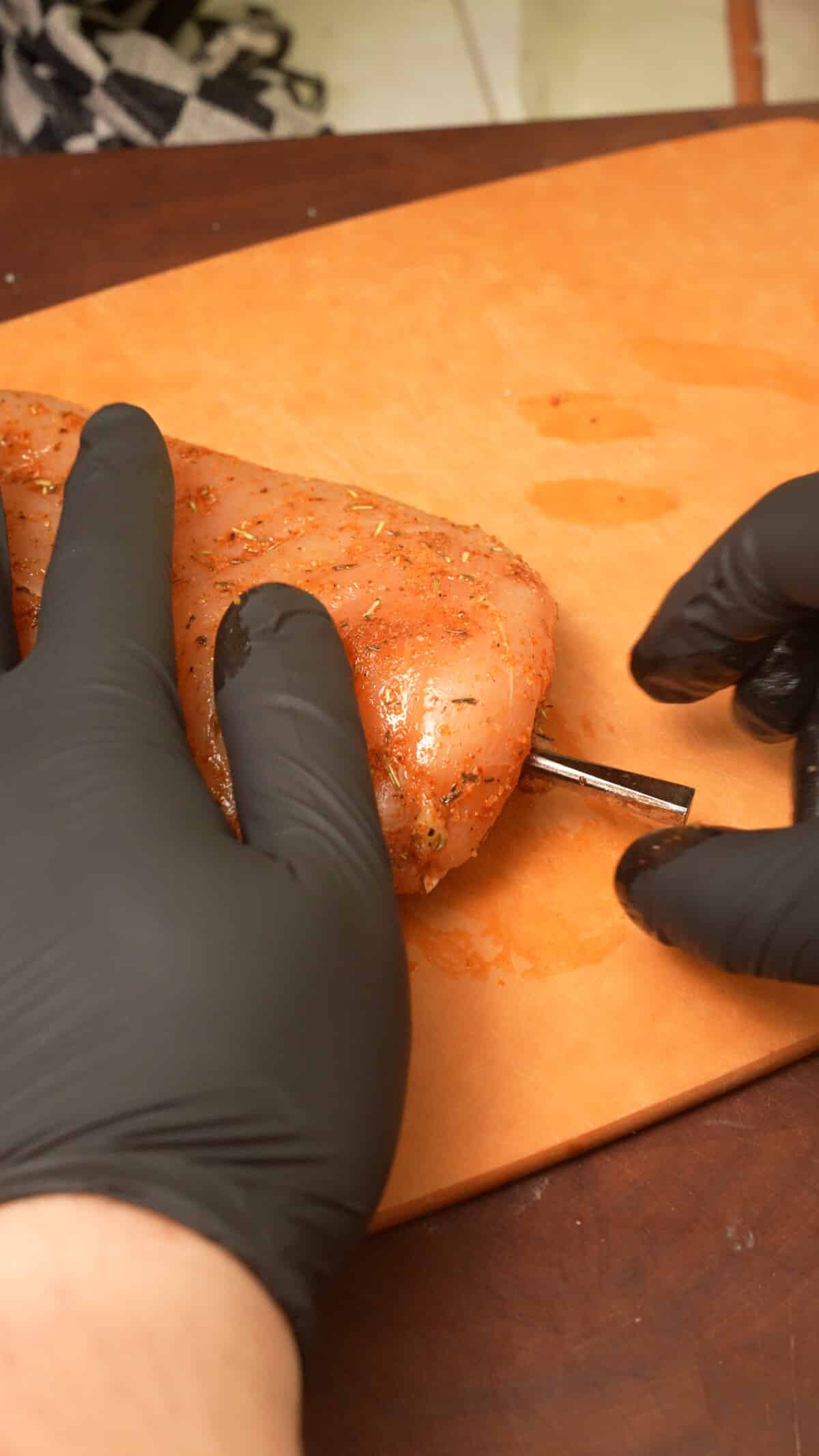 A thermometer probe placed in a chicken breast on a cutting board.