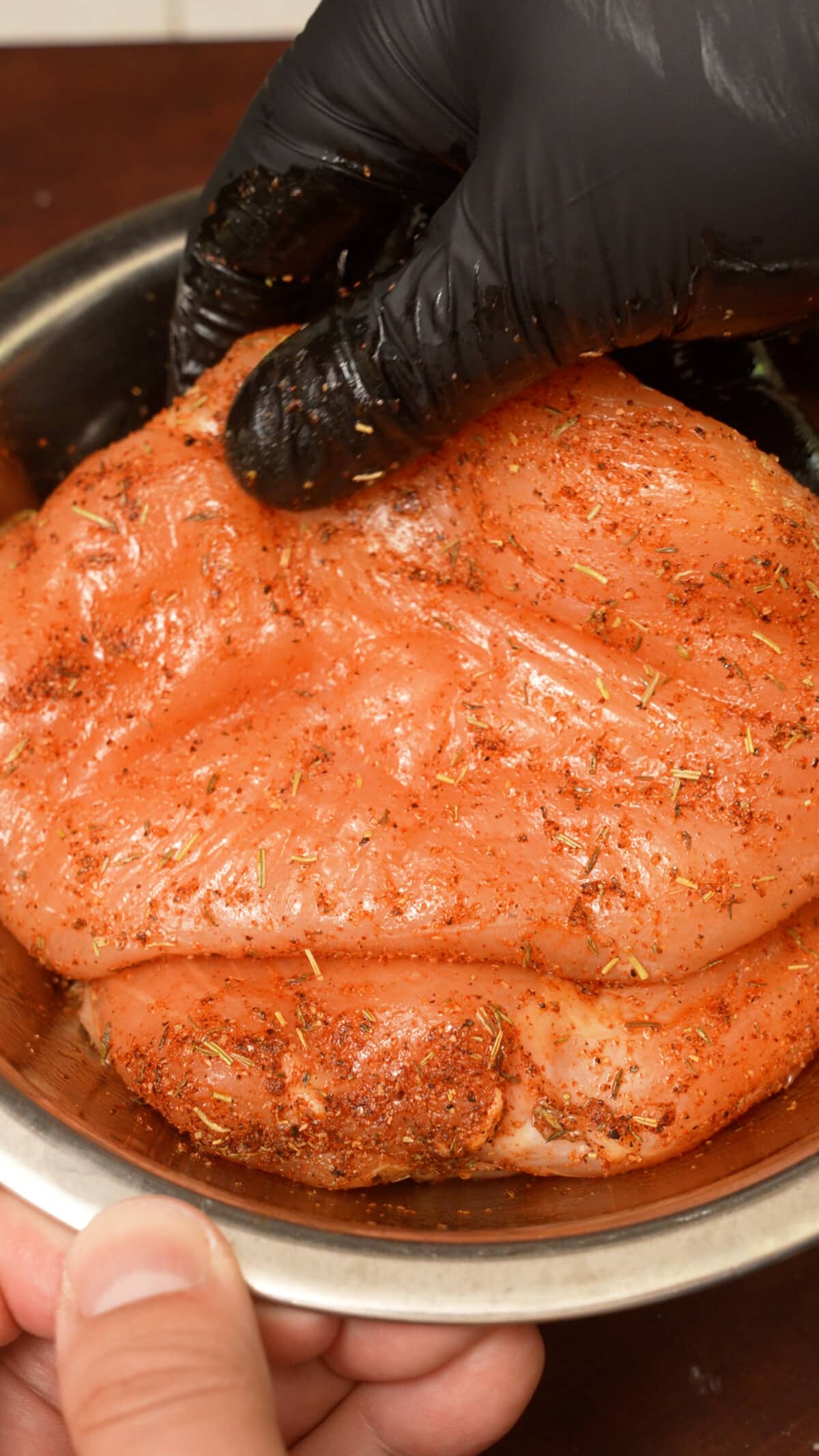 Raw chicken breasts marinated in a bowl.