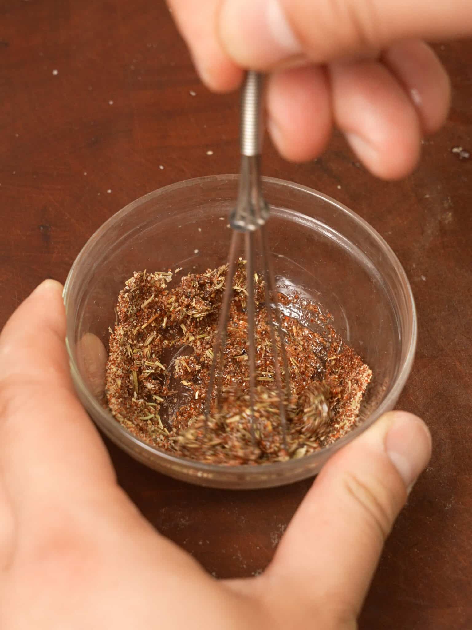 A small whisk mixing dry spices together in a small bowl.