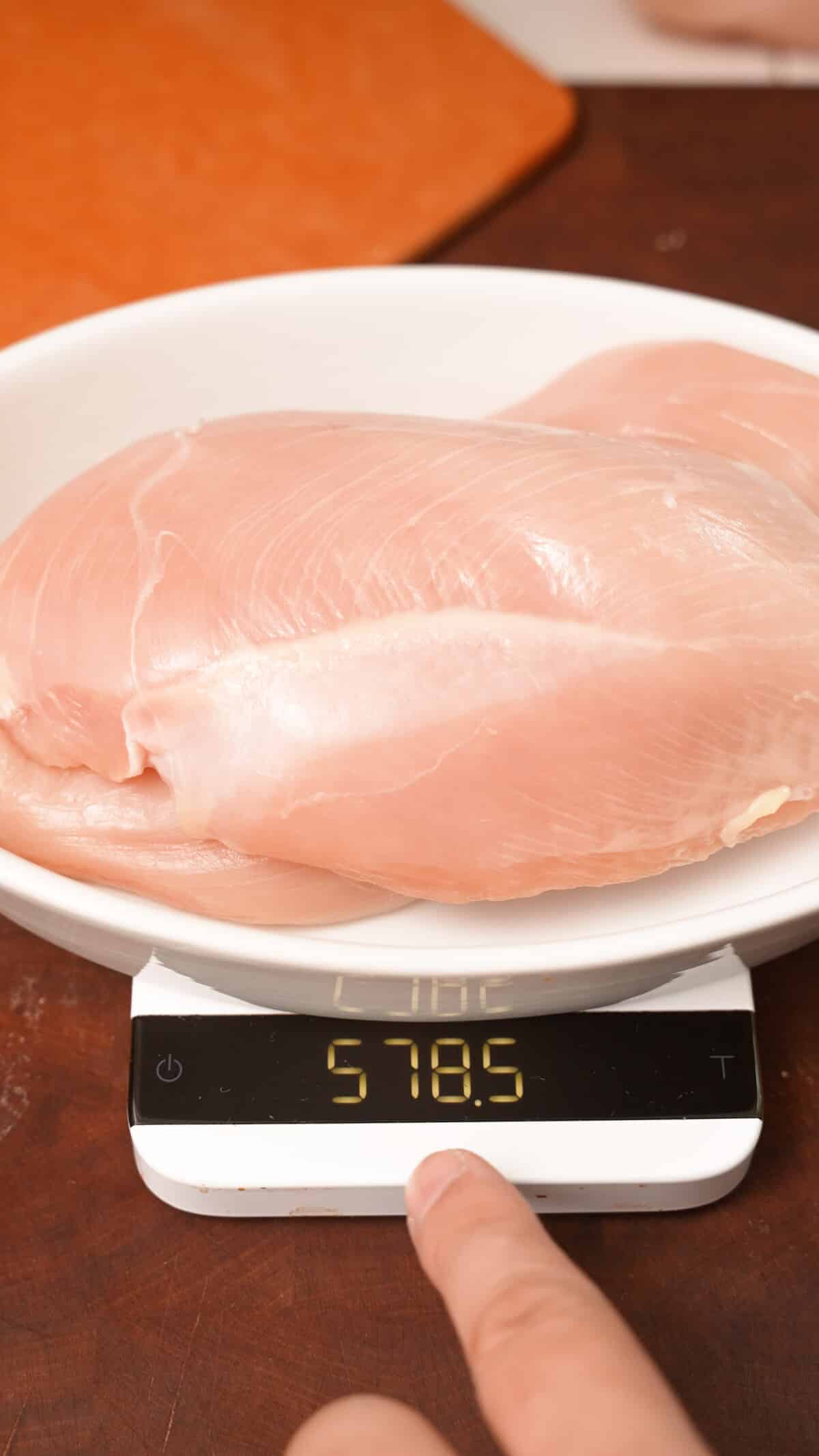 Chicken breasts being weighed on a scale in grams.