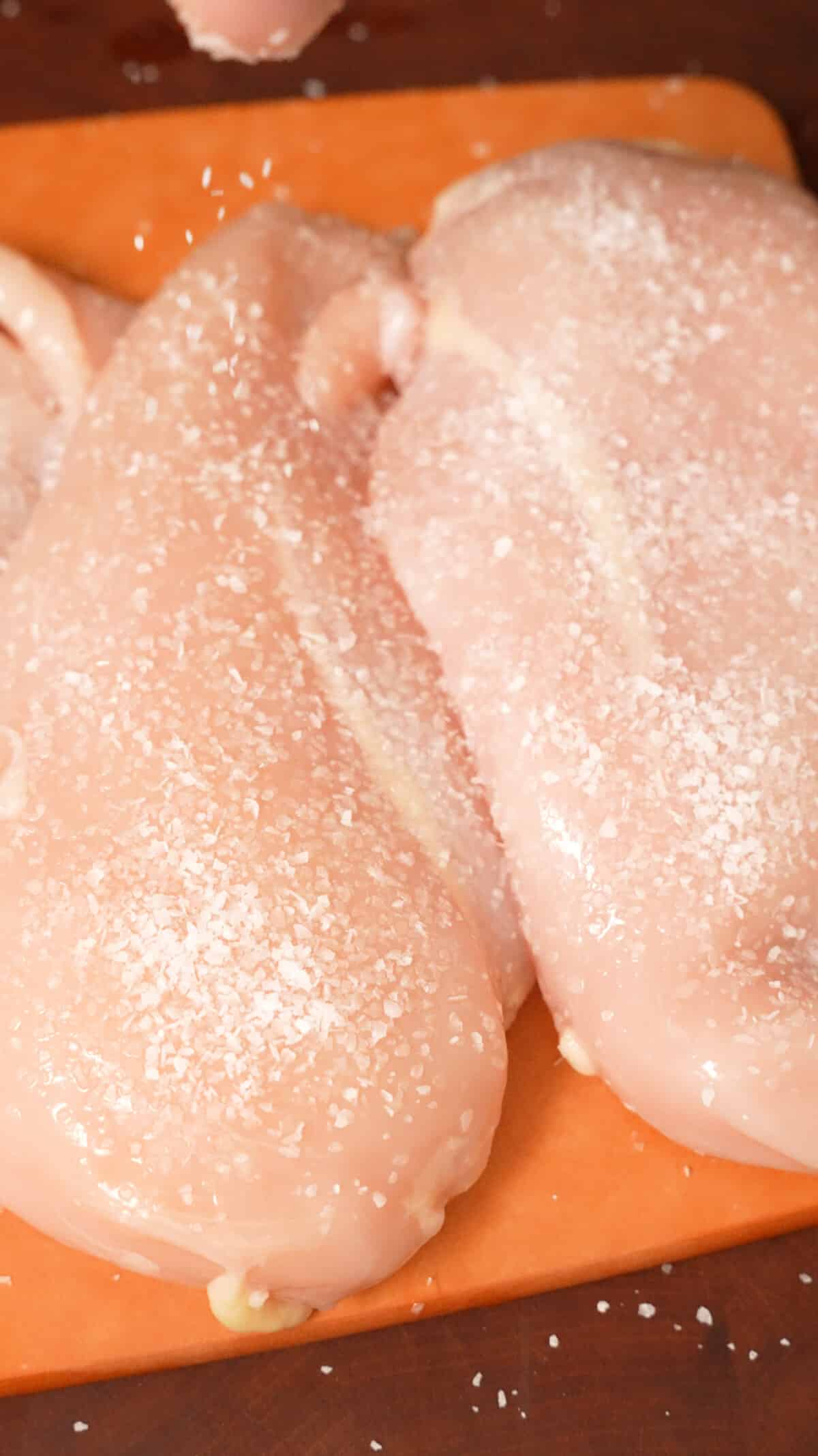 Kosher salt being sprinkled on chicken breasts for dry brining.