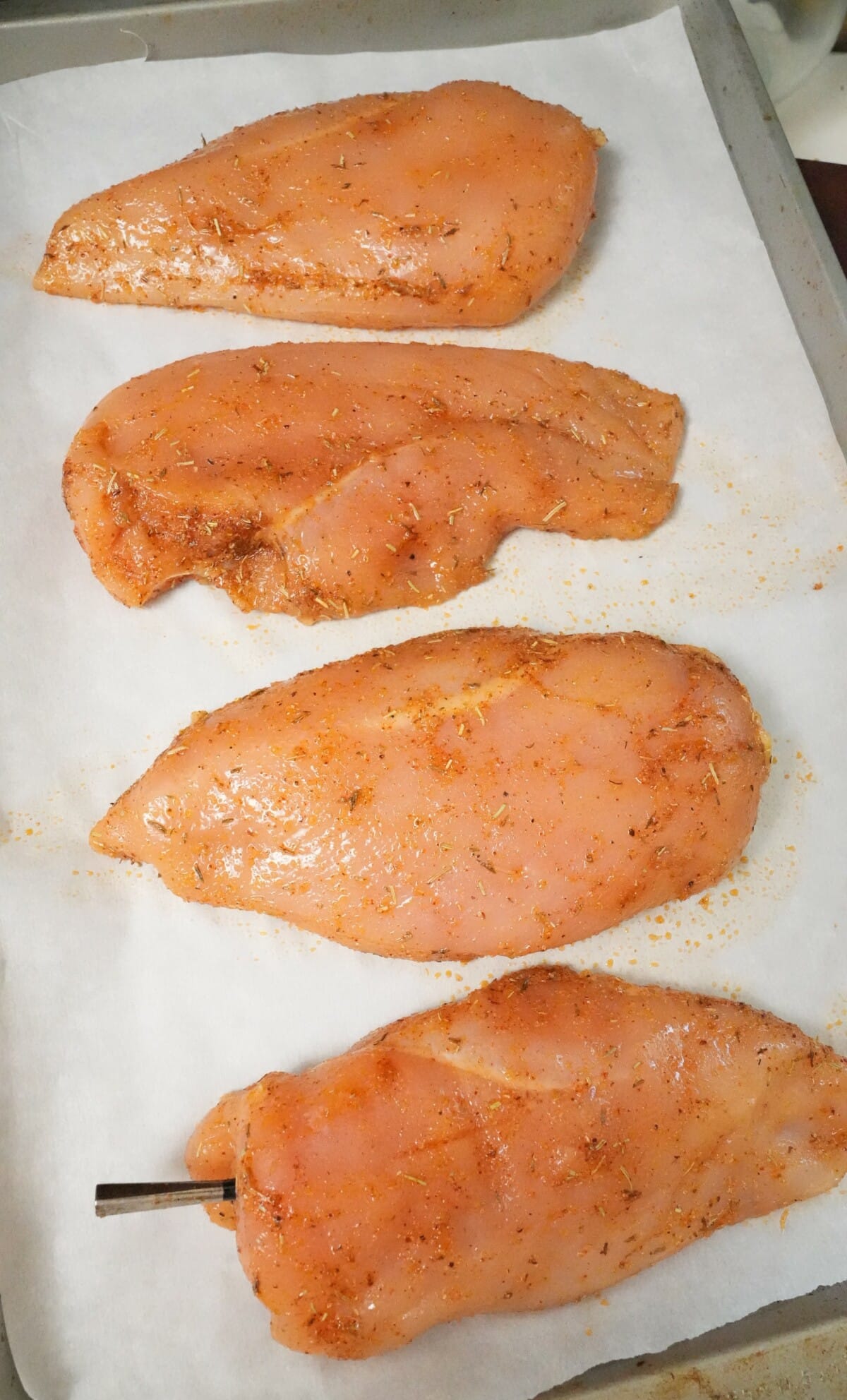 Raw chicken breasts on a parchment paper lined baking sheet before baking.