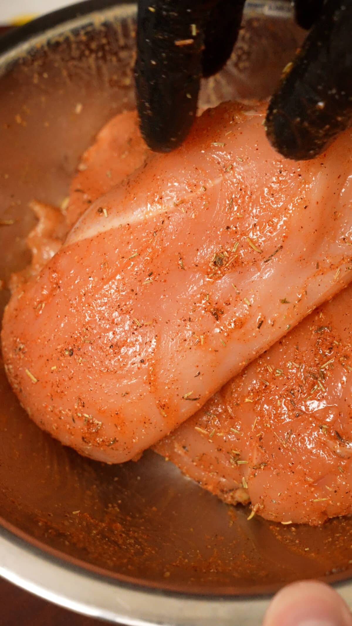 Raw chicken breasts marinated in the spice paste in a metal bowl.