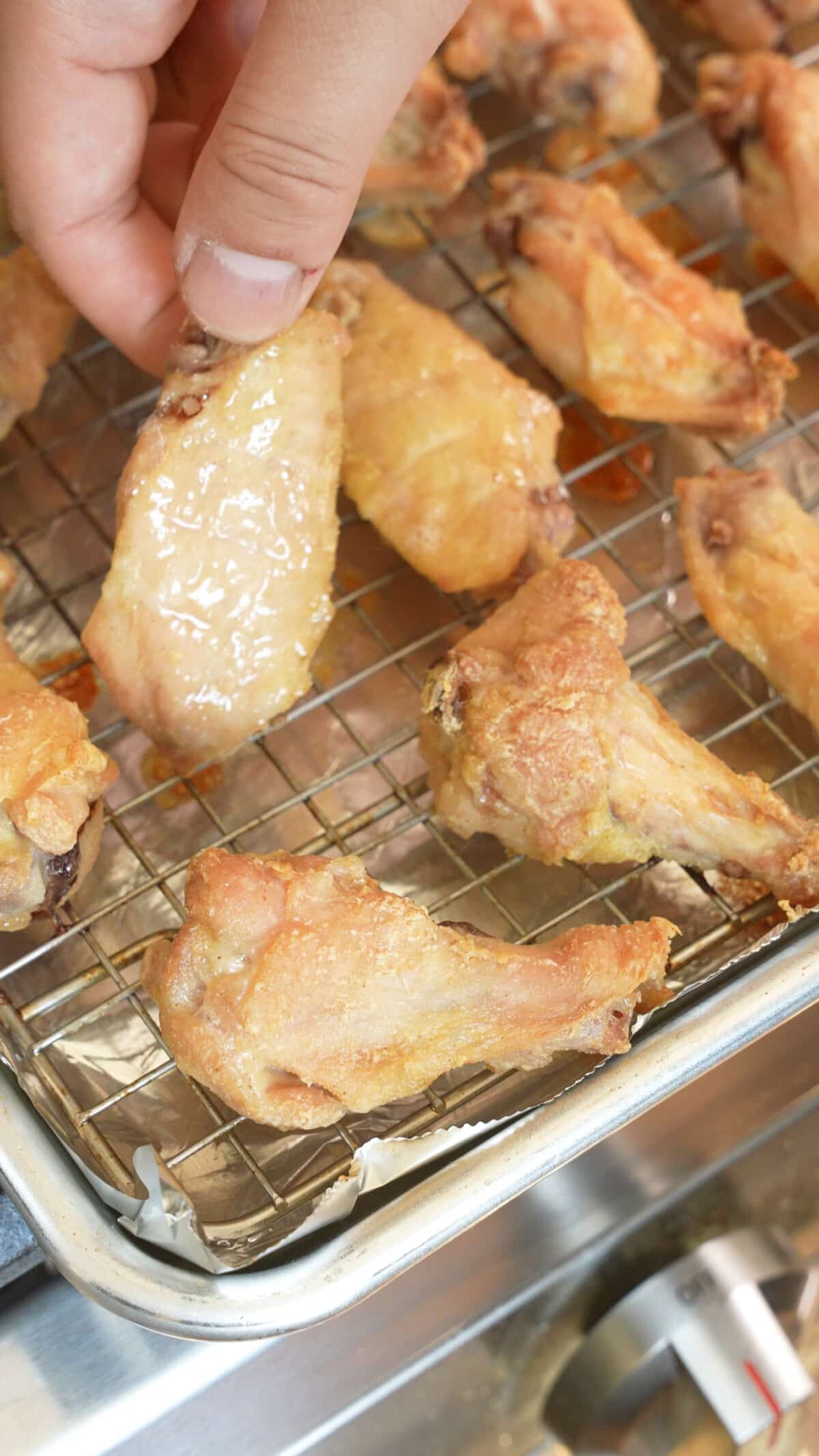 A hand flipping chicken wings on a wire rack.