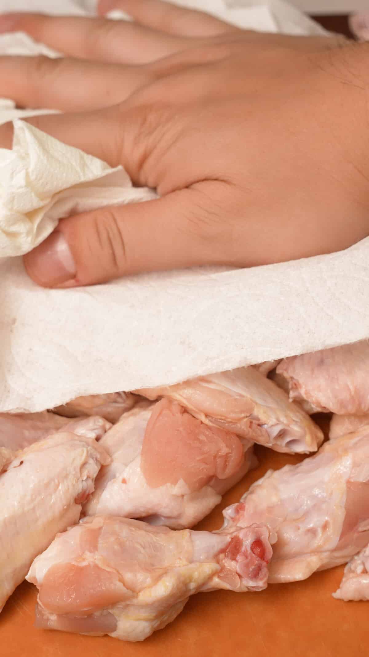 A hand patting dry chicken wings with a paper towel.