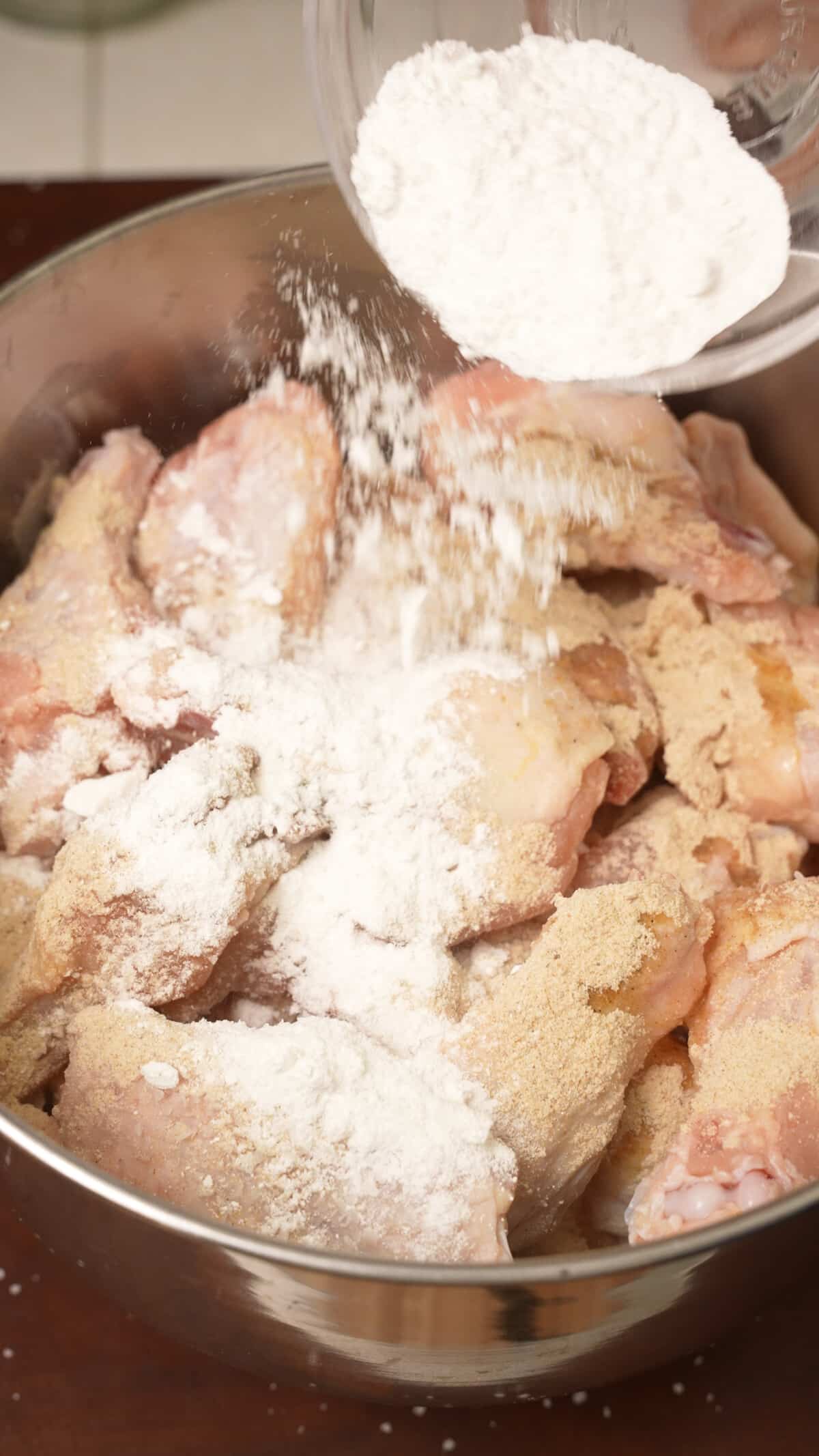 Baking powder being added to chicken wings in a metal bowl.