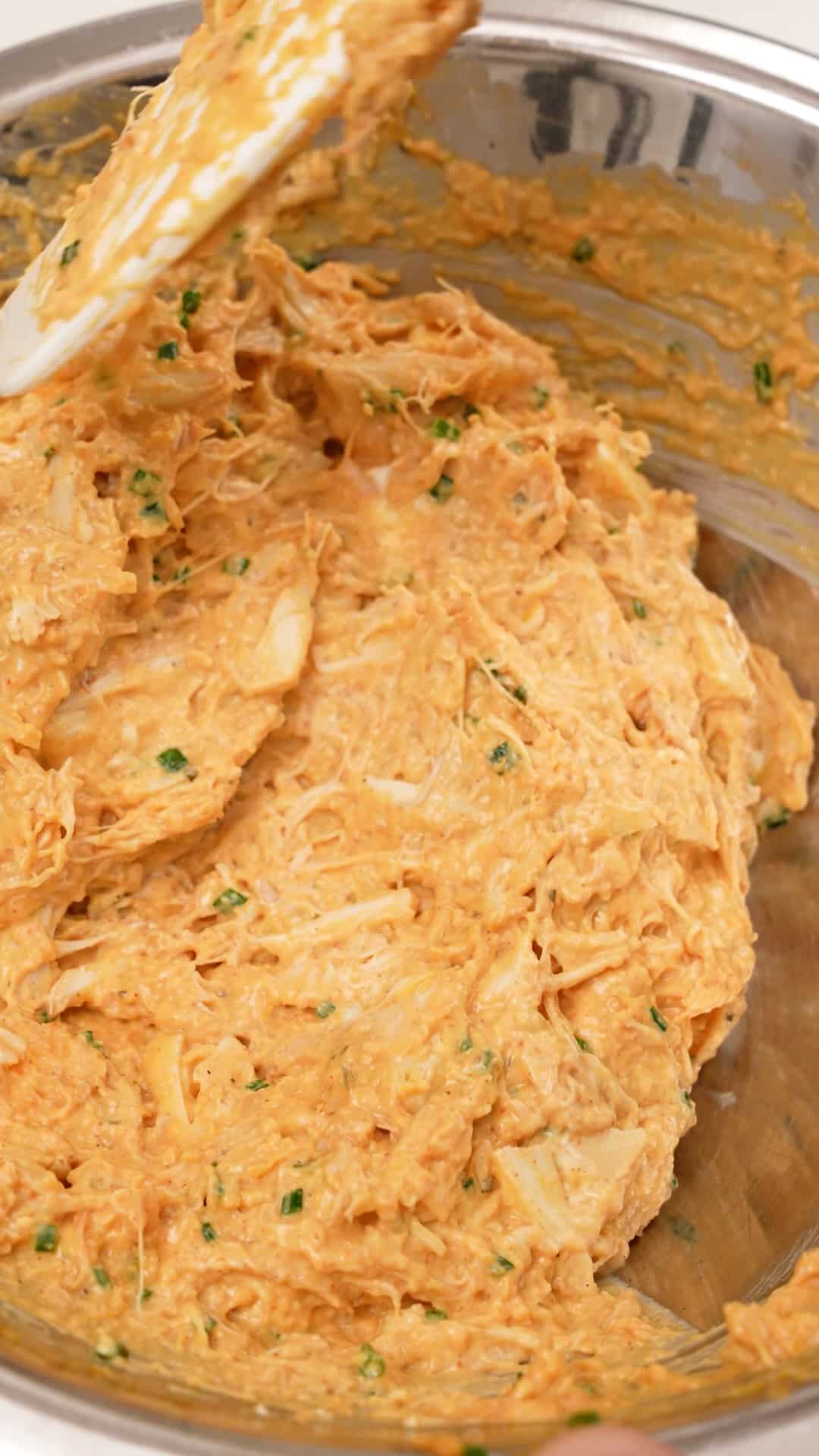 A spatula mixing baked crab dip in a metal bowl.