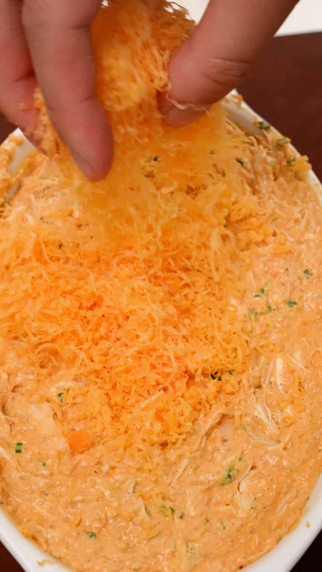 Adding cheese to baked crab dip in a tray.