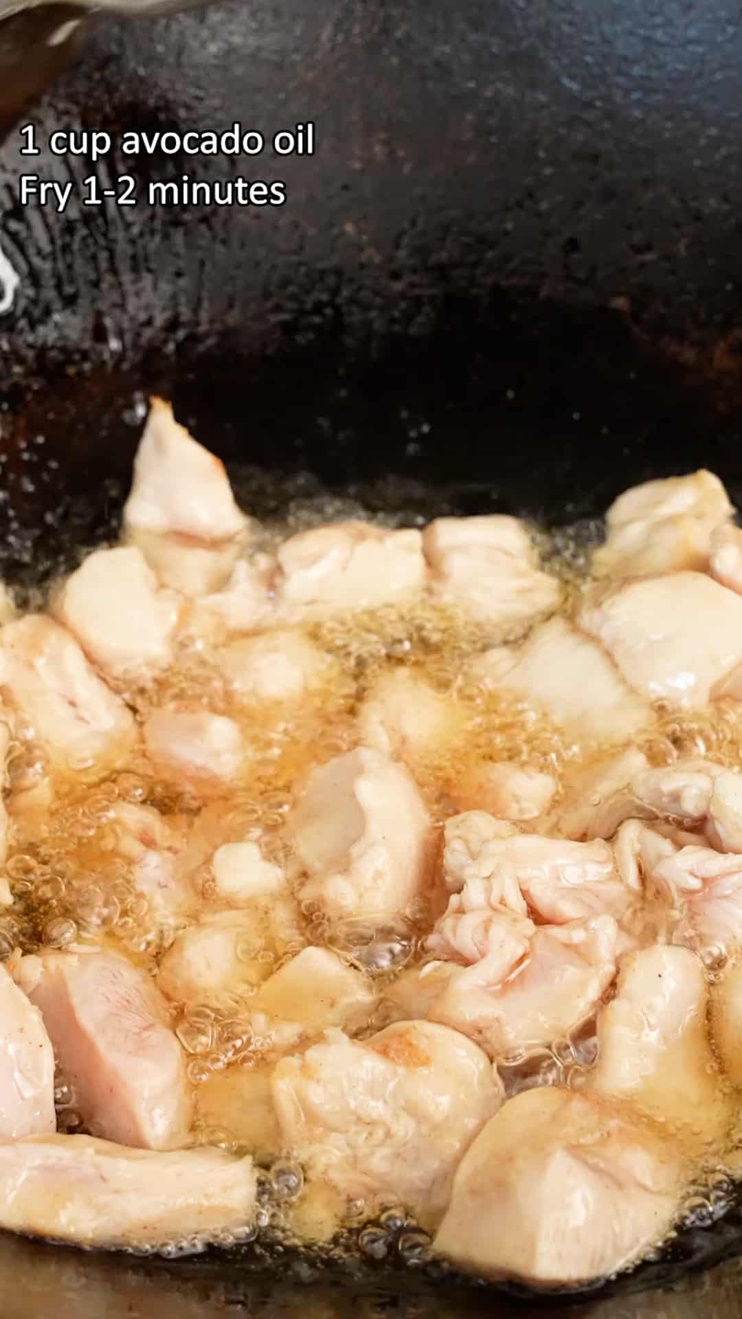 Pieces of chicken cooking in oil in a wok.