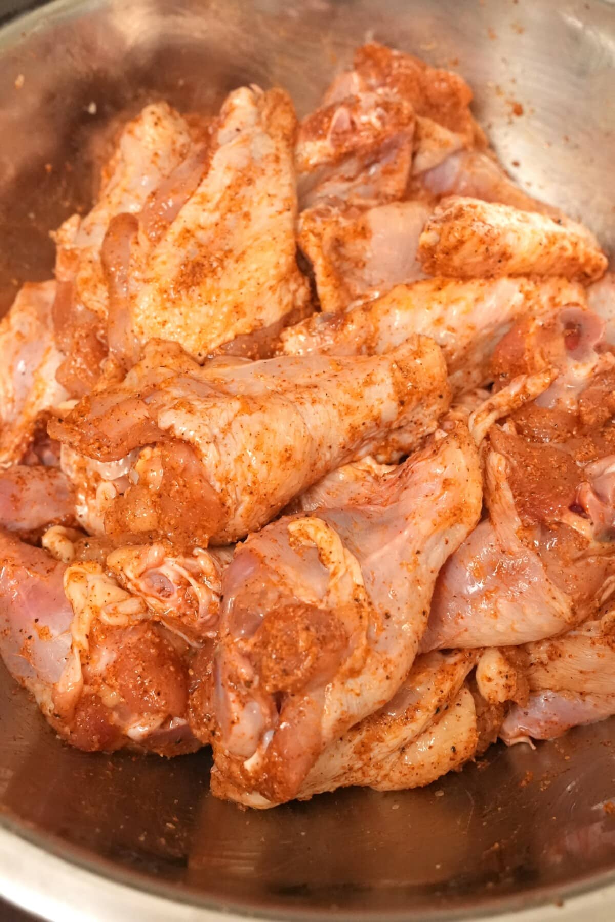 Seasoned chicken wings in a metal bowl with dry spices and baking powder.