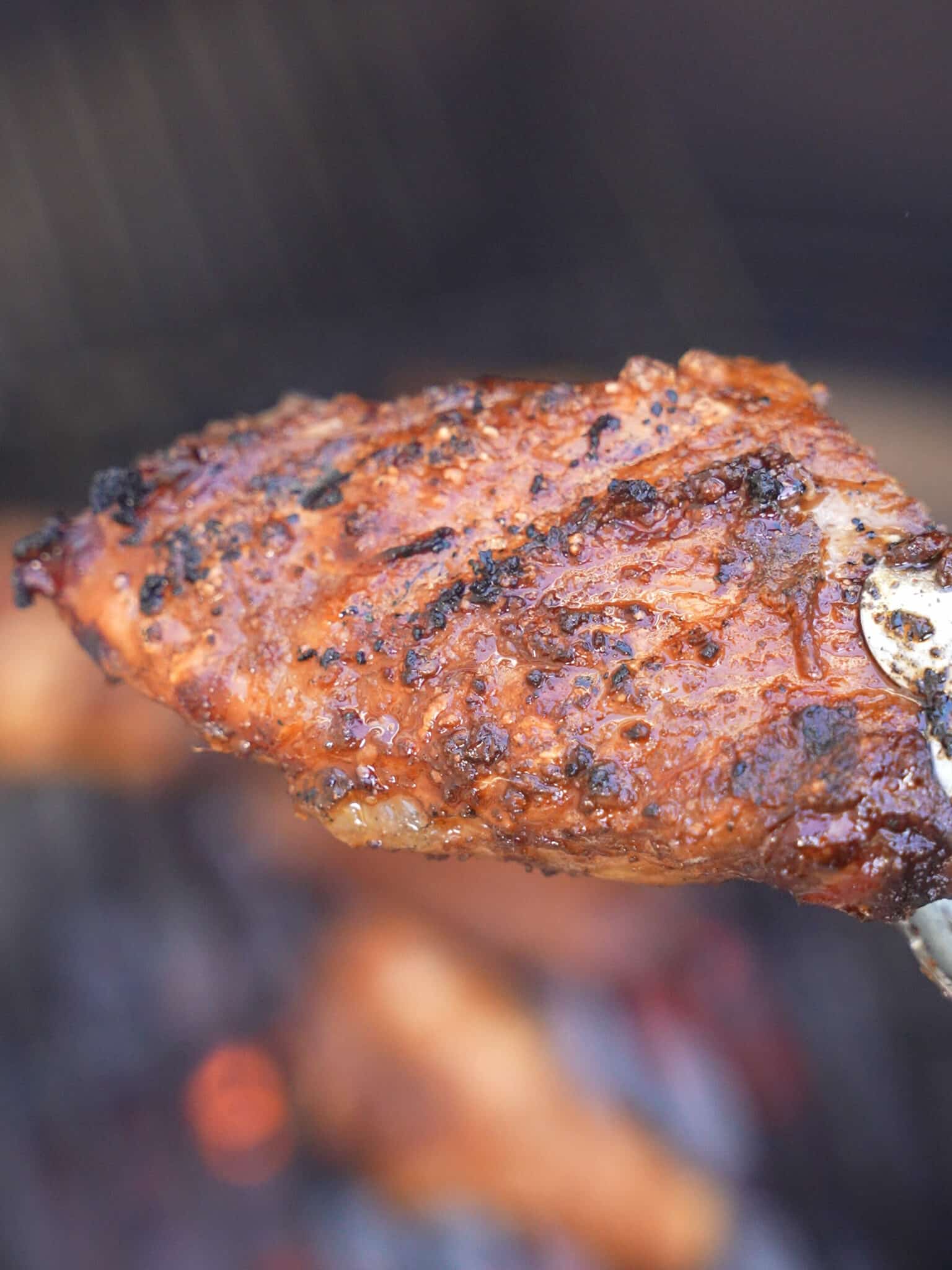 A pair of tongs holding up a grilled chicken wing after searing over direct charcoals.