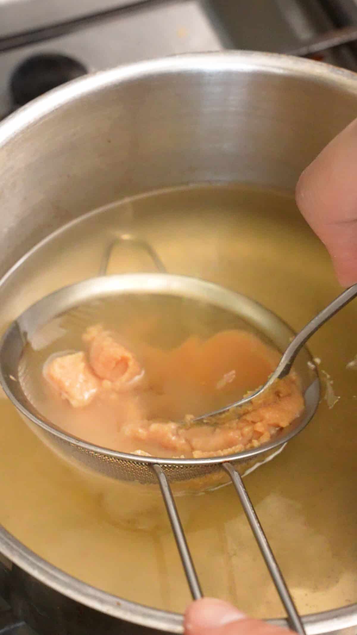 White miso paste being dissolved through a mesh strainer into dashi broth.