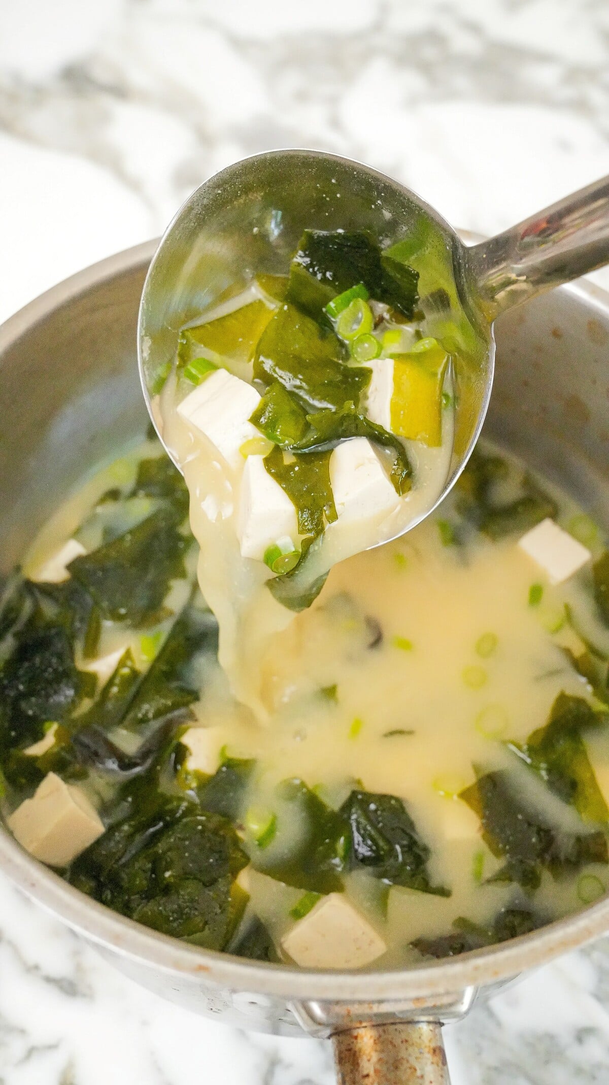 A ladle pouring miso soup in a pot.