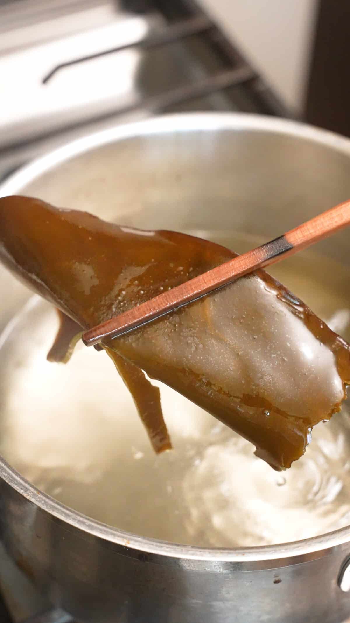 A pair of chopsticks removing konbu from the water after simmering.