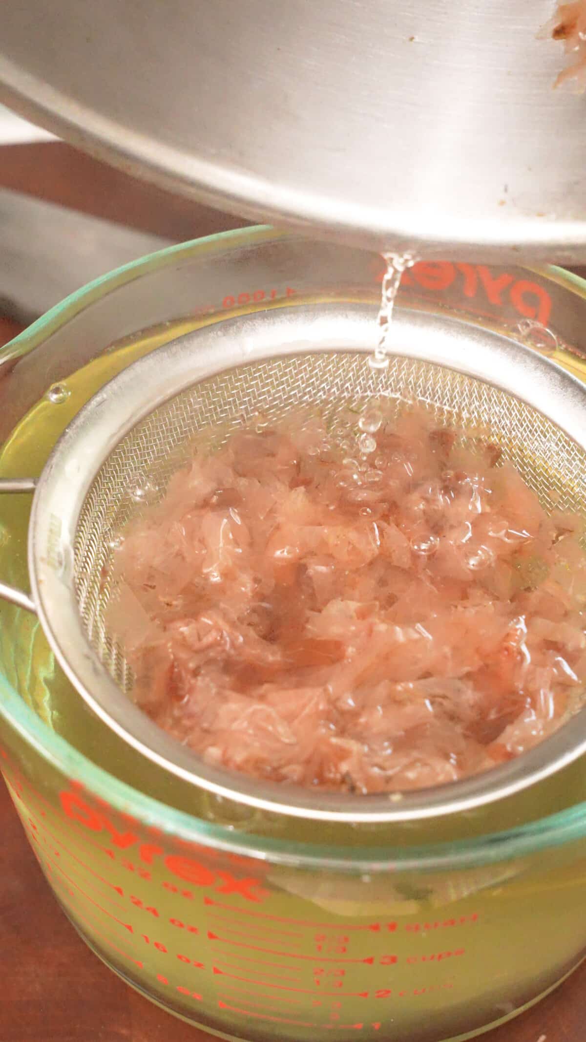 Straining the bonito flakes from the dashi broth with a mesh strainer.