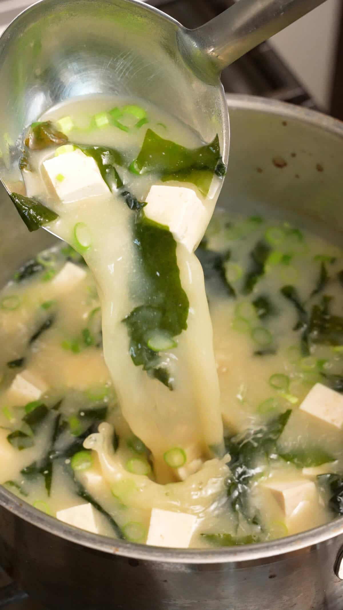 A ladle pouring Miso soup in a pot on the stove.