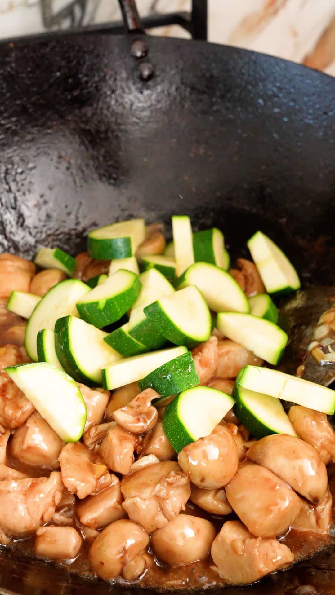 Zucchini added to the mushroom chicken in a wok.