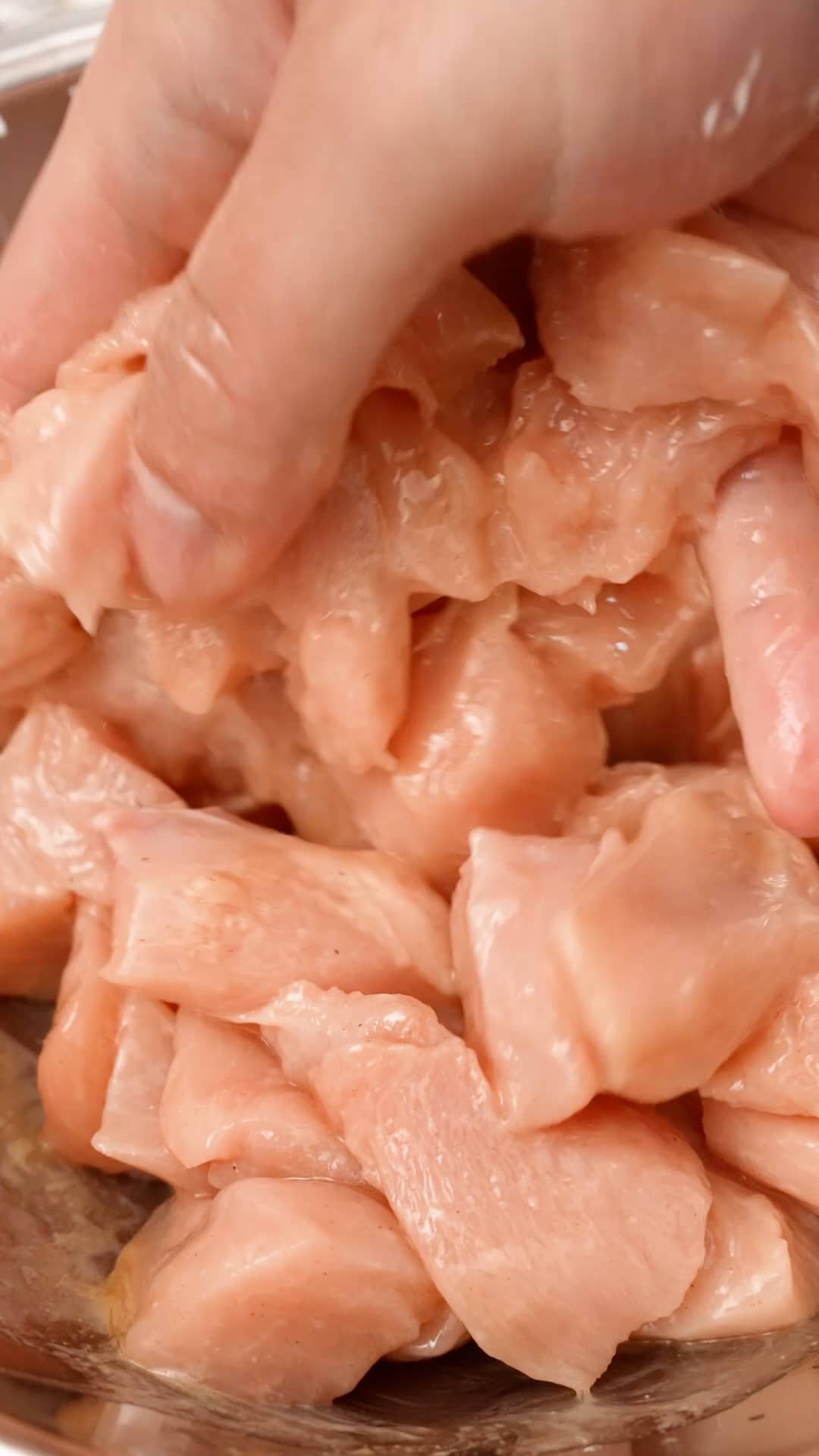 A hand marinating chicken breast in a metal bowl.