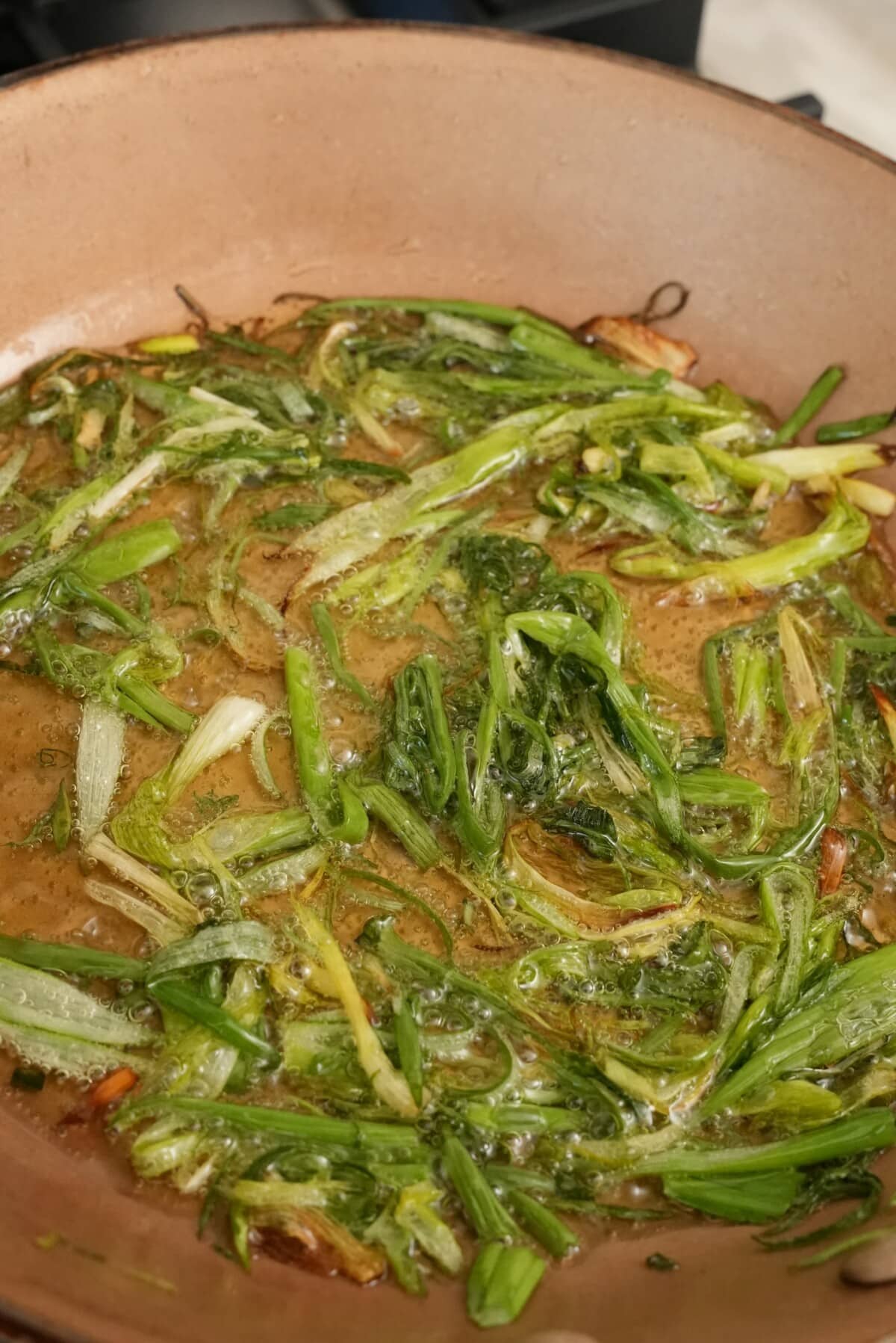 Scallion greens frying in oil in a pan.