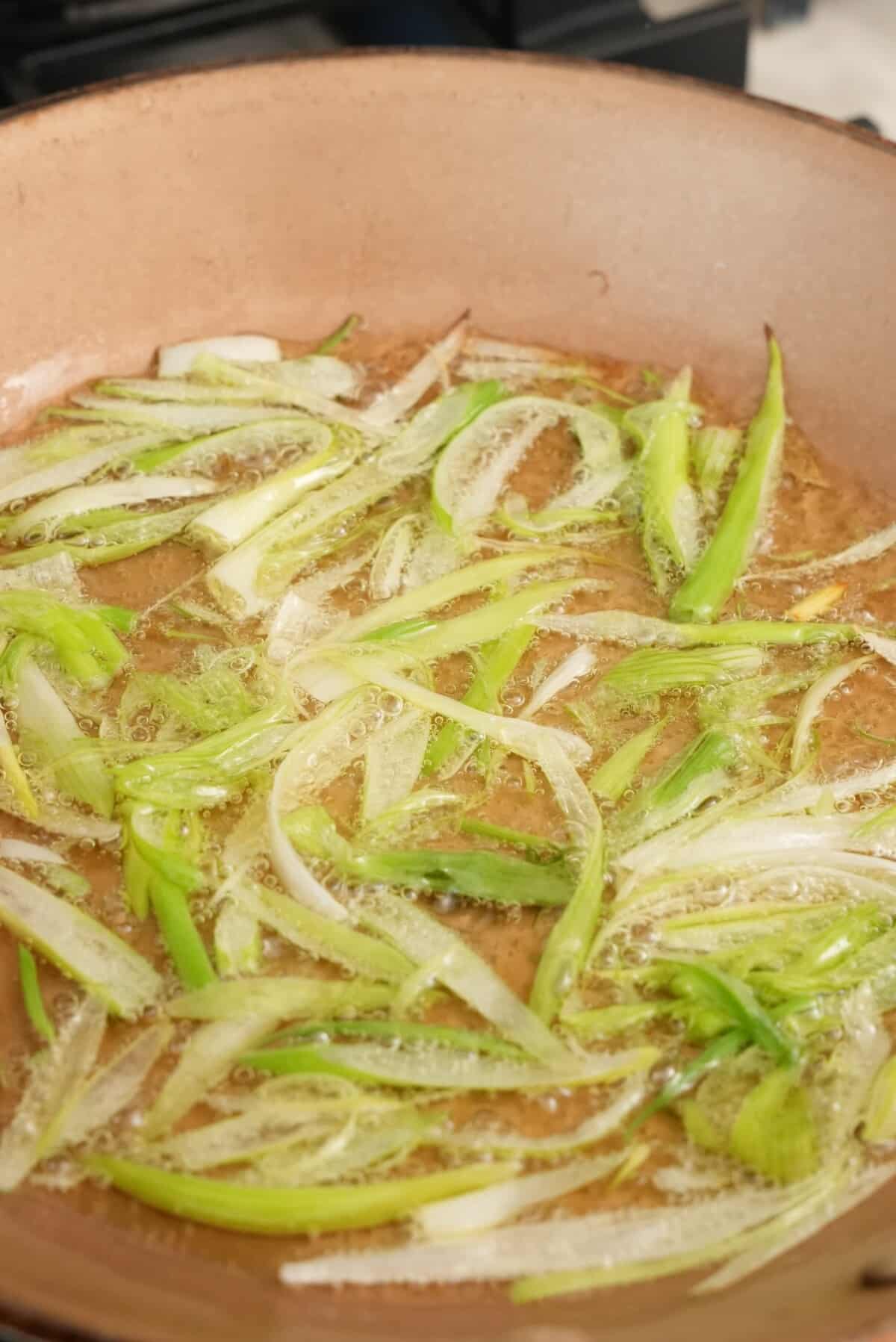 Scallion whites frying in oil in a pan.