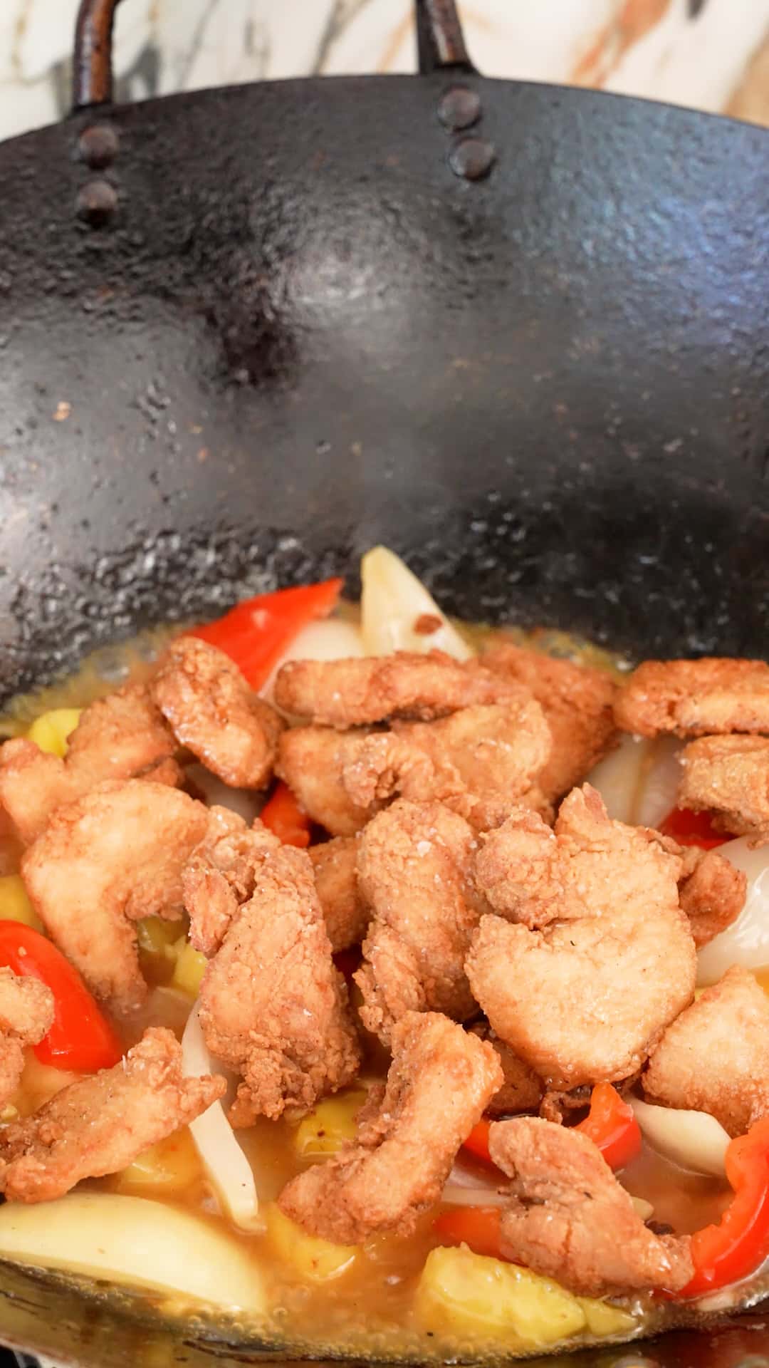 Fried chicken breast added back into the wok with peppers, onions, pineapple and sauce