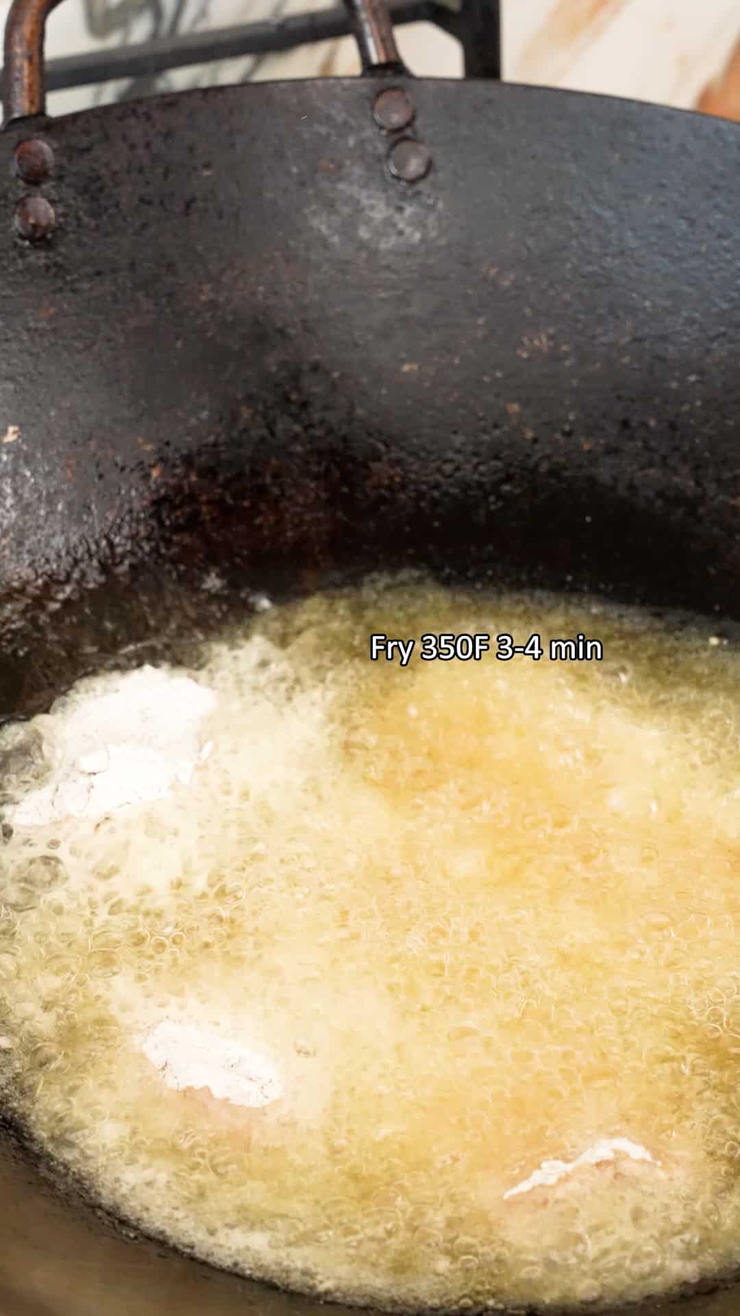 Chicken pieces frying in oil in a wok.