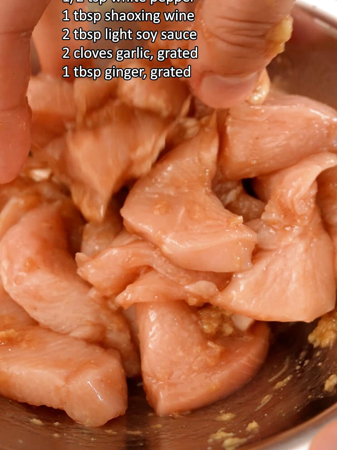 Chicken breast marinating in a metal bowl.