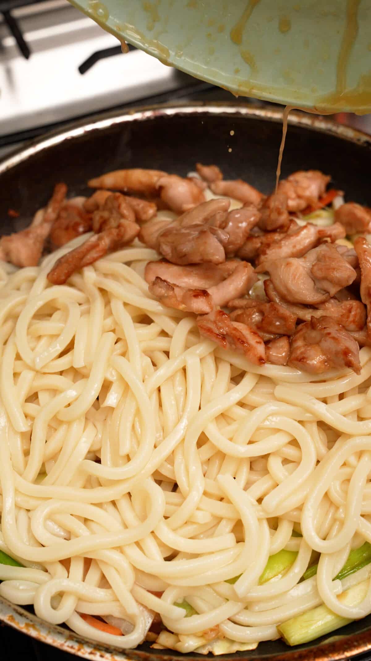 Udon noodles and chicken being added to the pan.