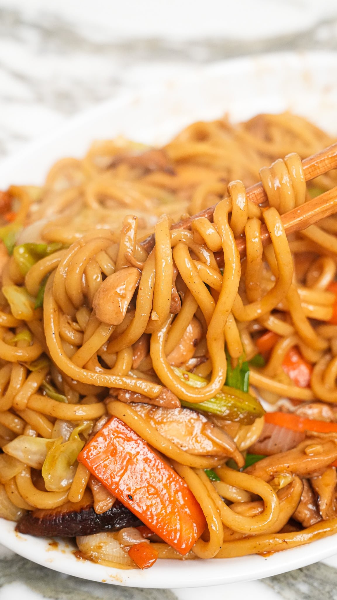 A pair of chopsticks holding up Yaki Udon on a tray.