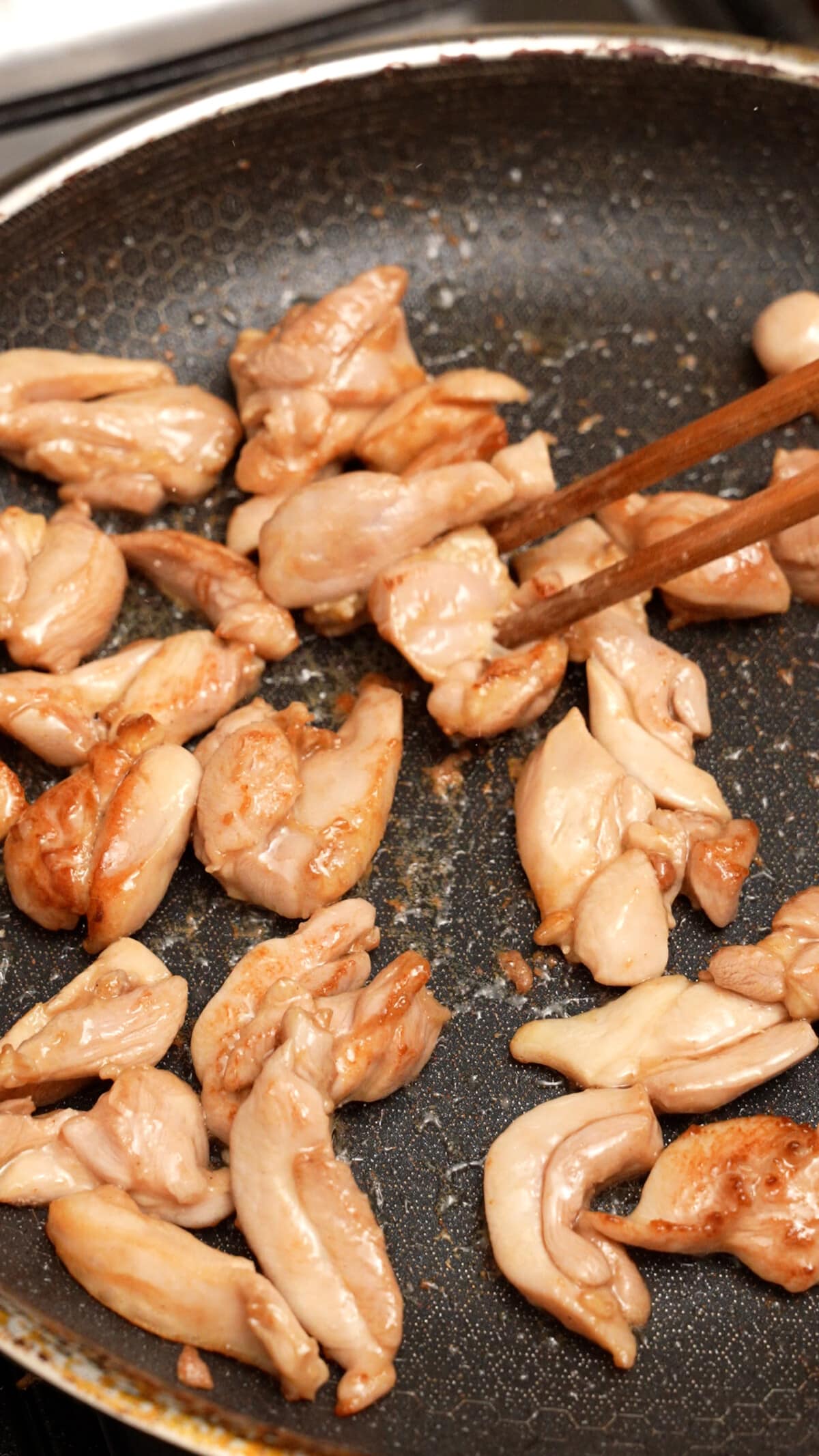 Chicken pieces cooking in a pan.