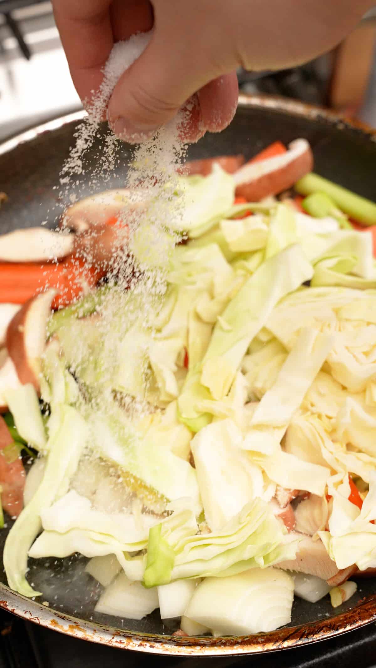 Kosher salt being added to vegetables cooking in a pan.