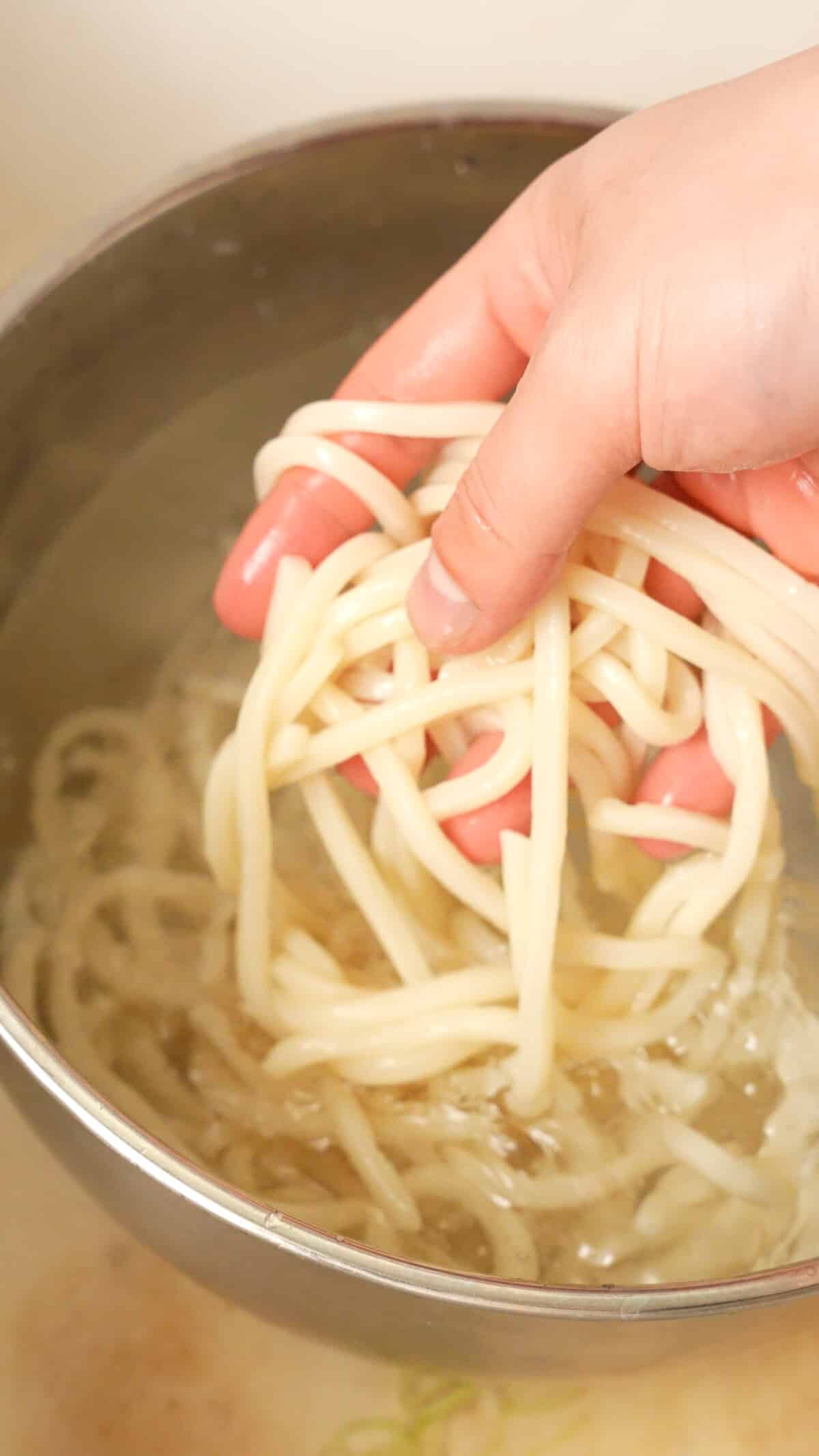 Frozen udon noodles defrosting in a bowl of water being separated by hand.