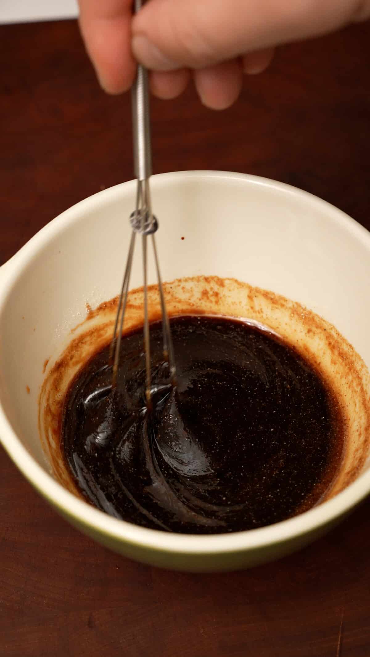 A small whisk mixing stir fry sauce in a bowl.