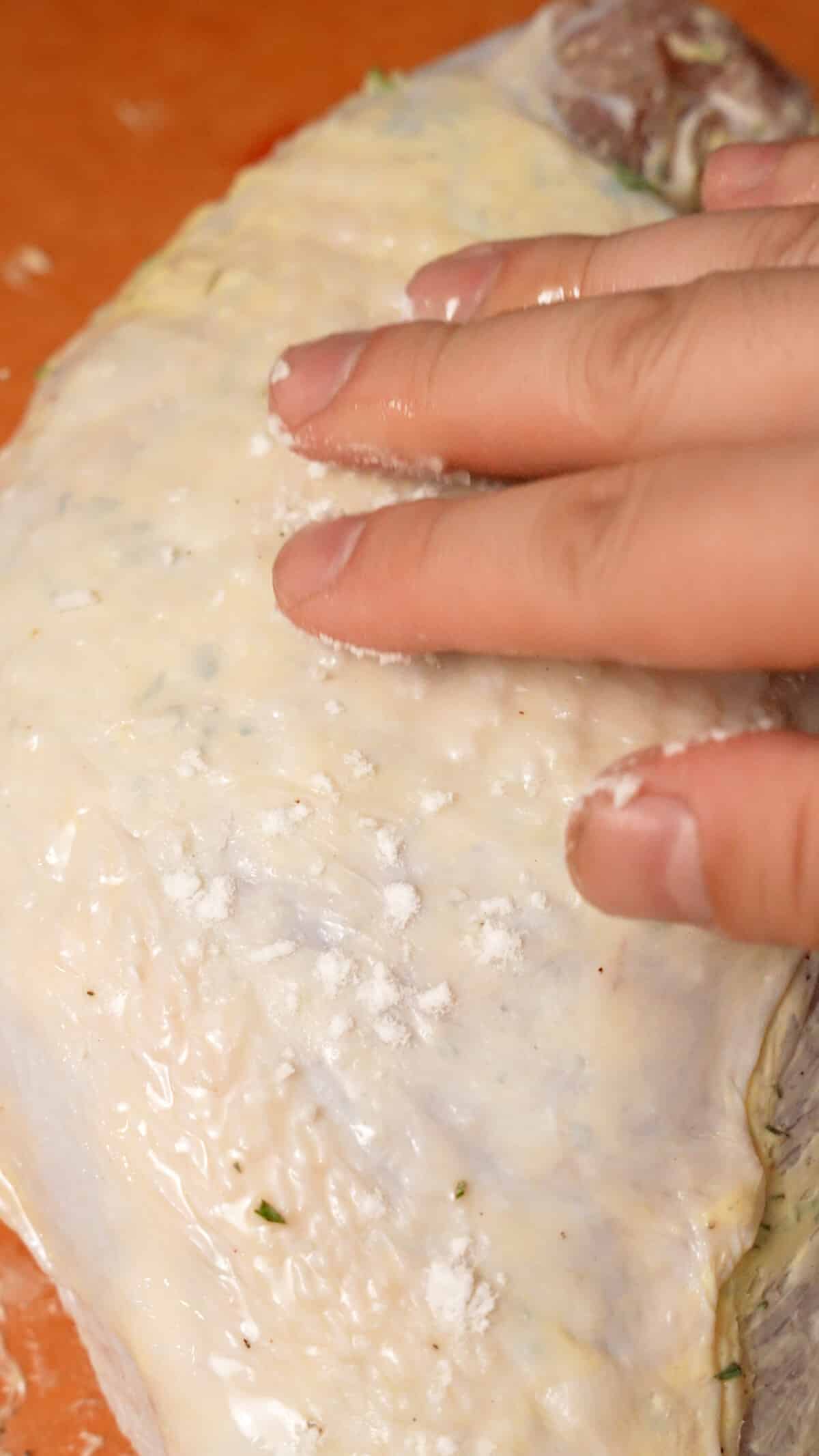 A hand rubbing baking powder into the skin of a turkey breast.