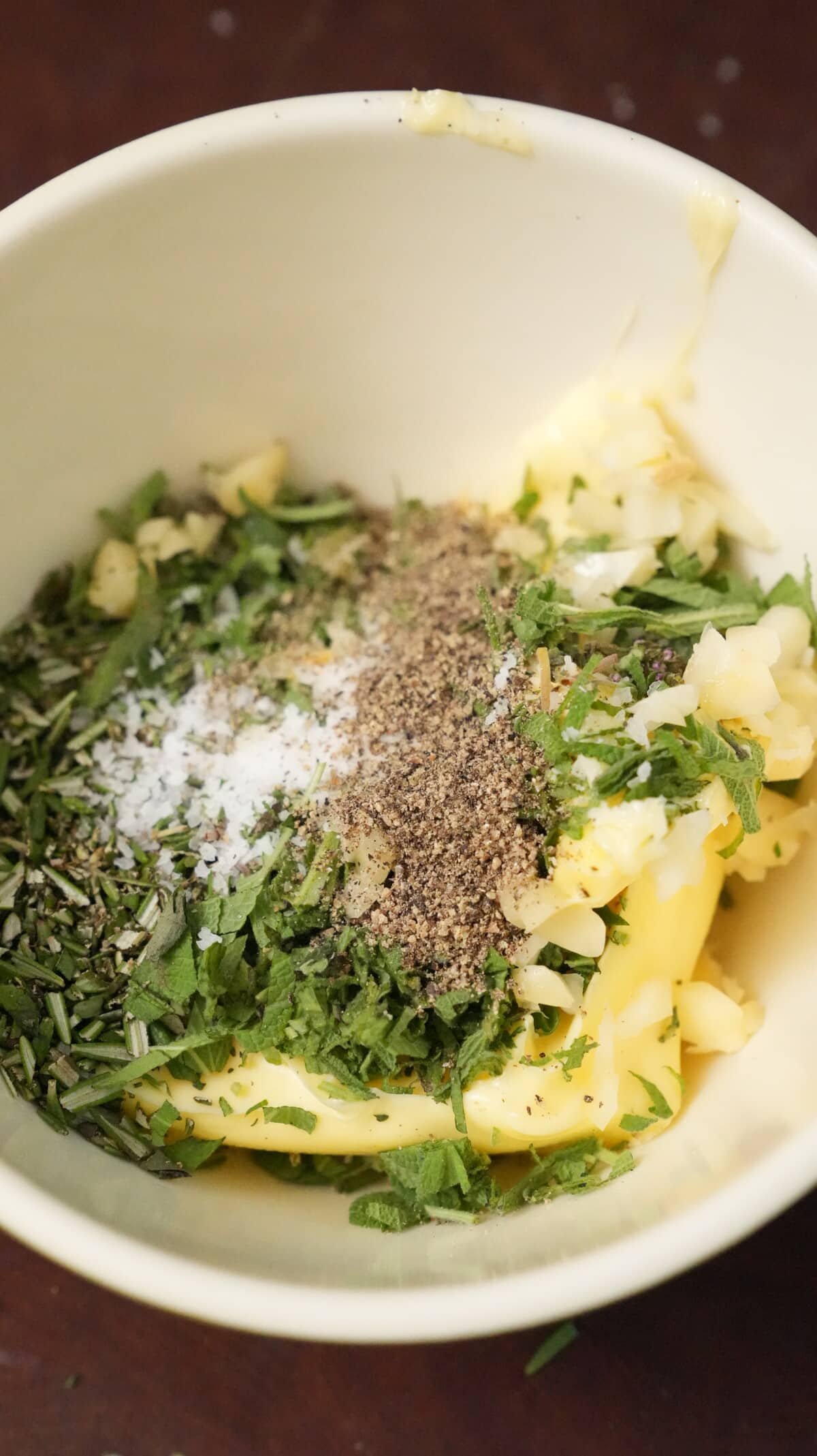 Compound butter in a bowl with garlic, thyme, rosemary, and sage.