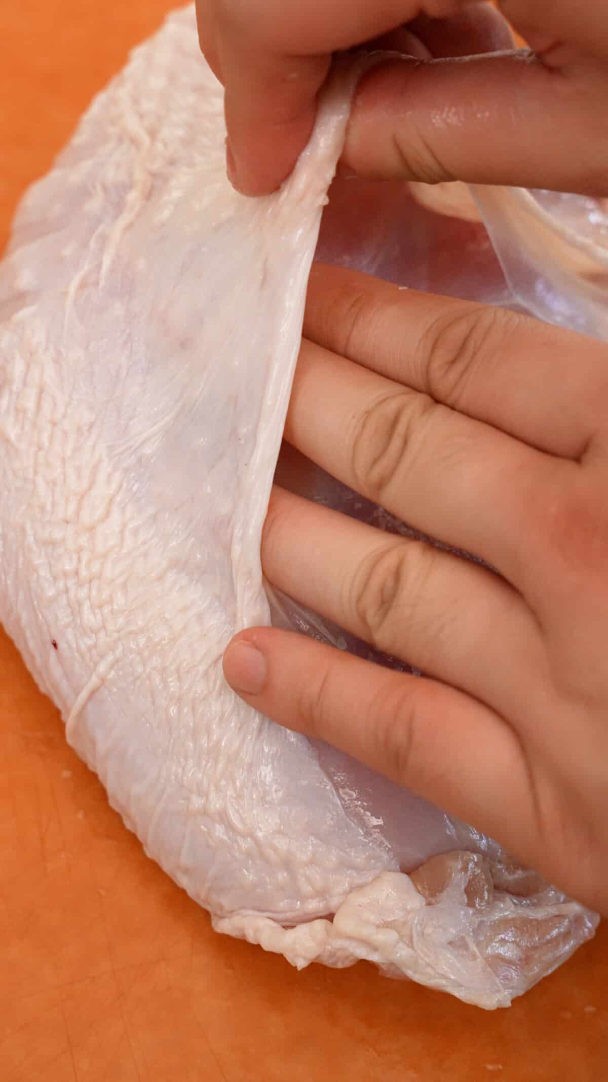 A hand gently separating the skin from the turkey breast meat.