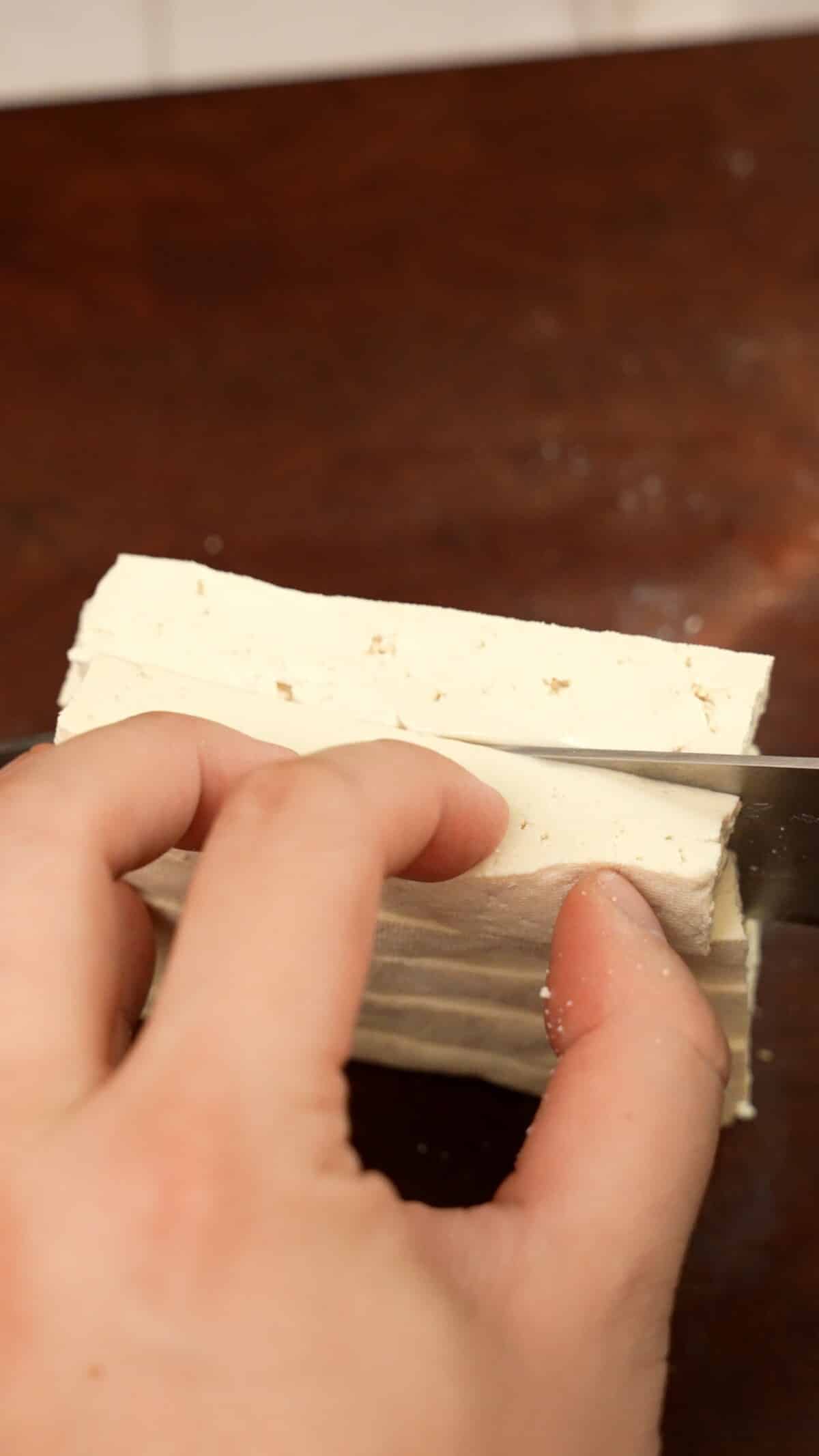 A knife slicing tofu slabs in half.