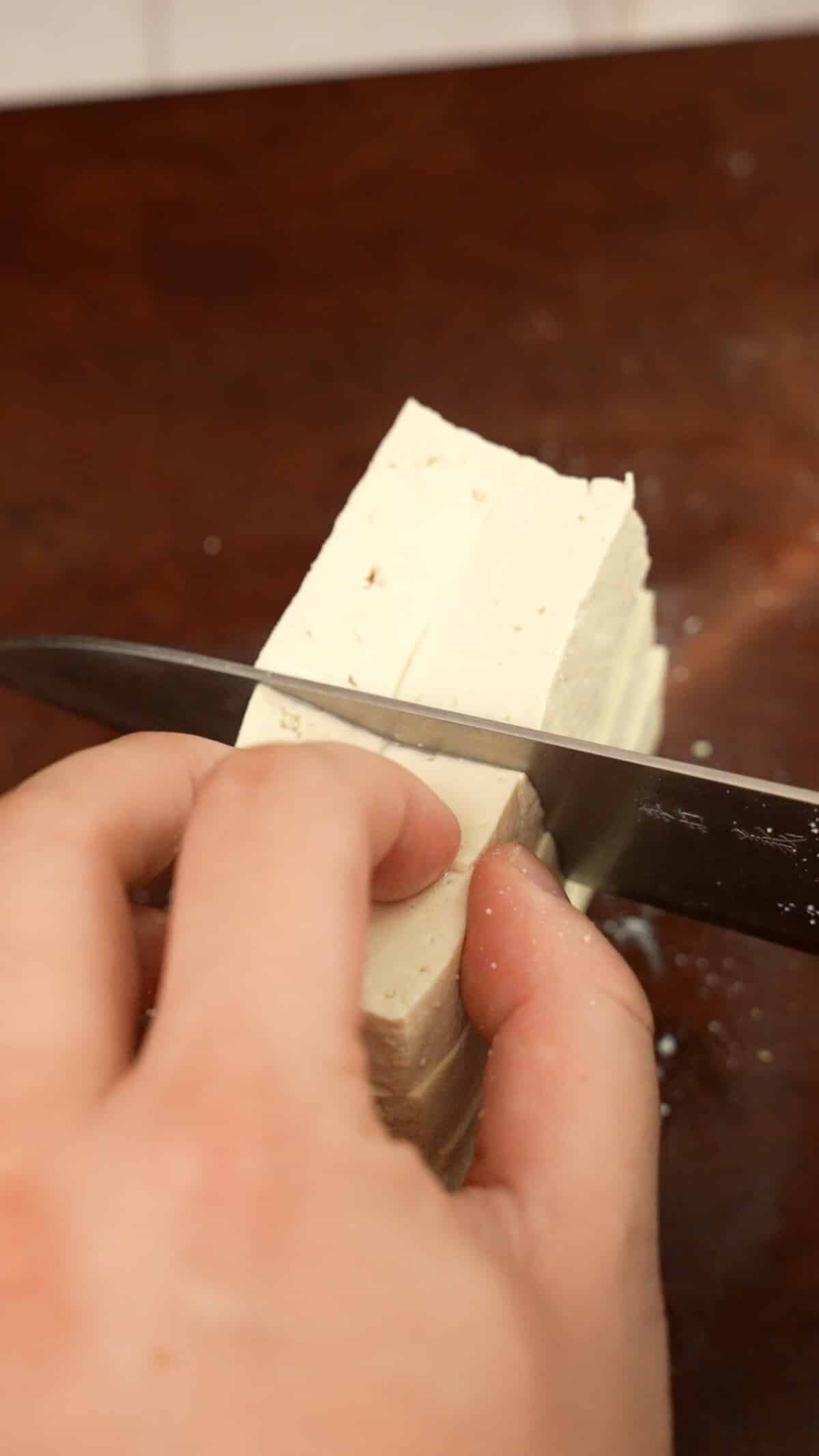 Slicing tofu into cubes on a cutting board.