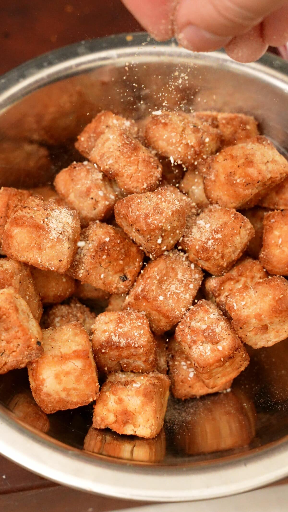 Dry seasoning being sprinkled onto crispy tofu cubes.