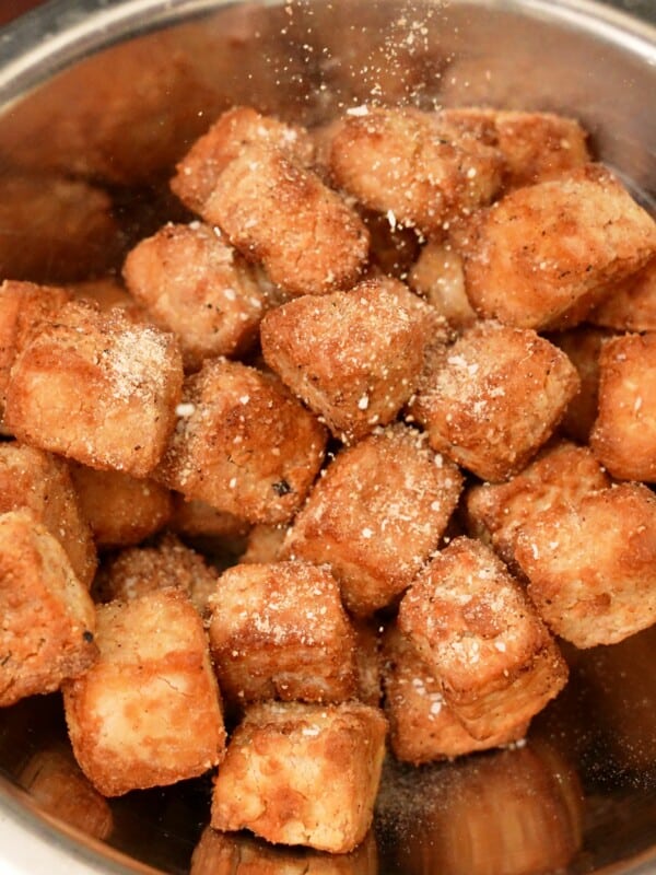 Dry seasoning being sprinkled onto crispy tofu cubes.