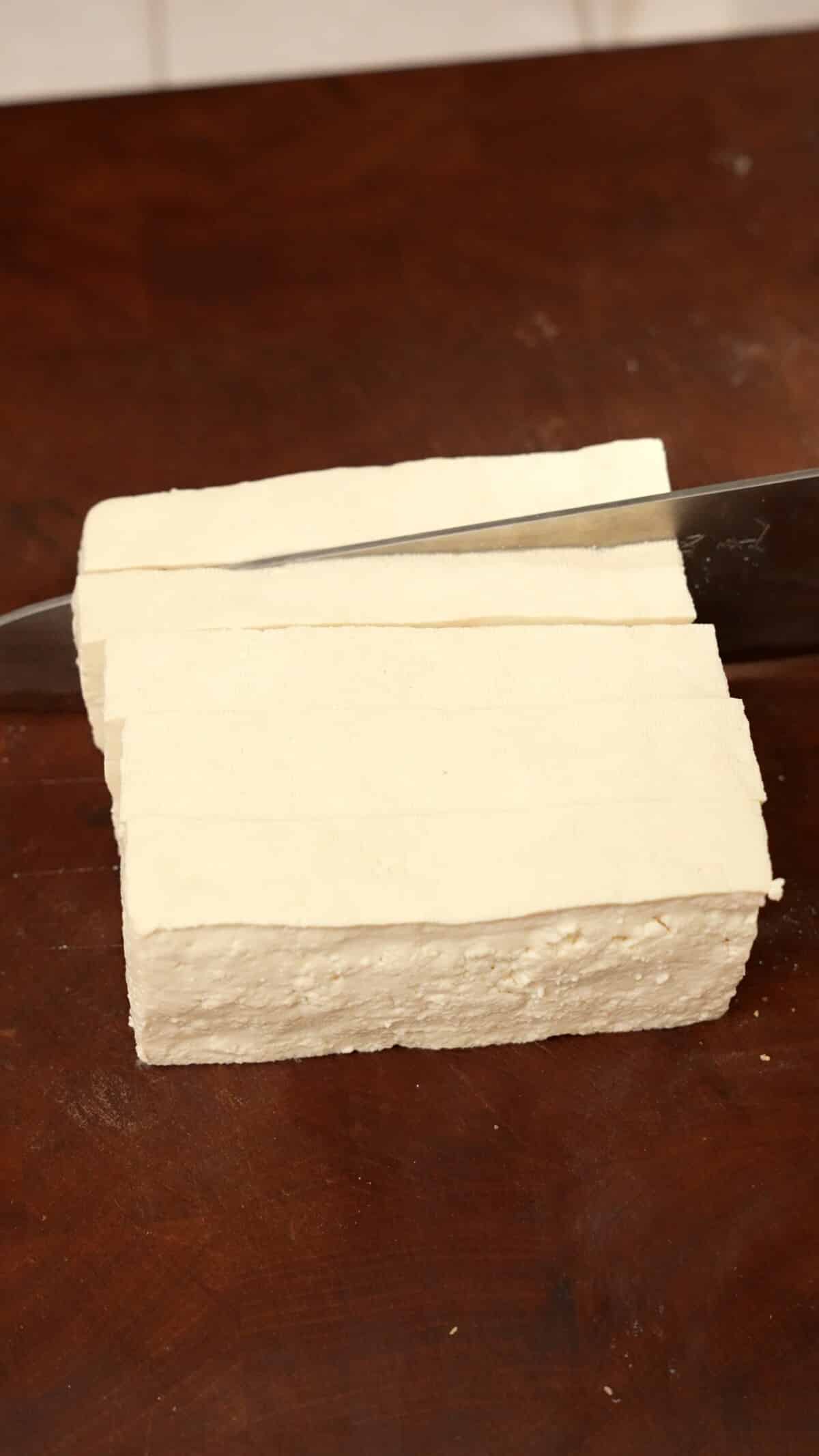 Tofu being sliced into 1 inch slabs.