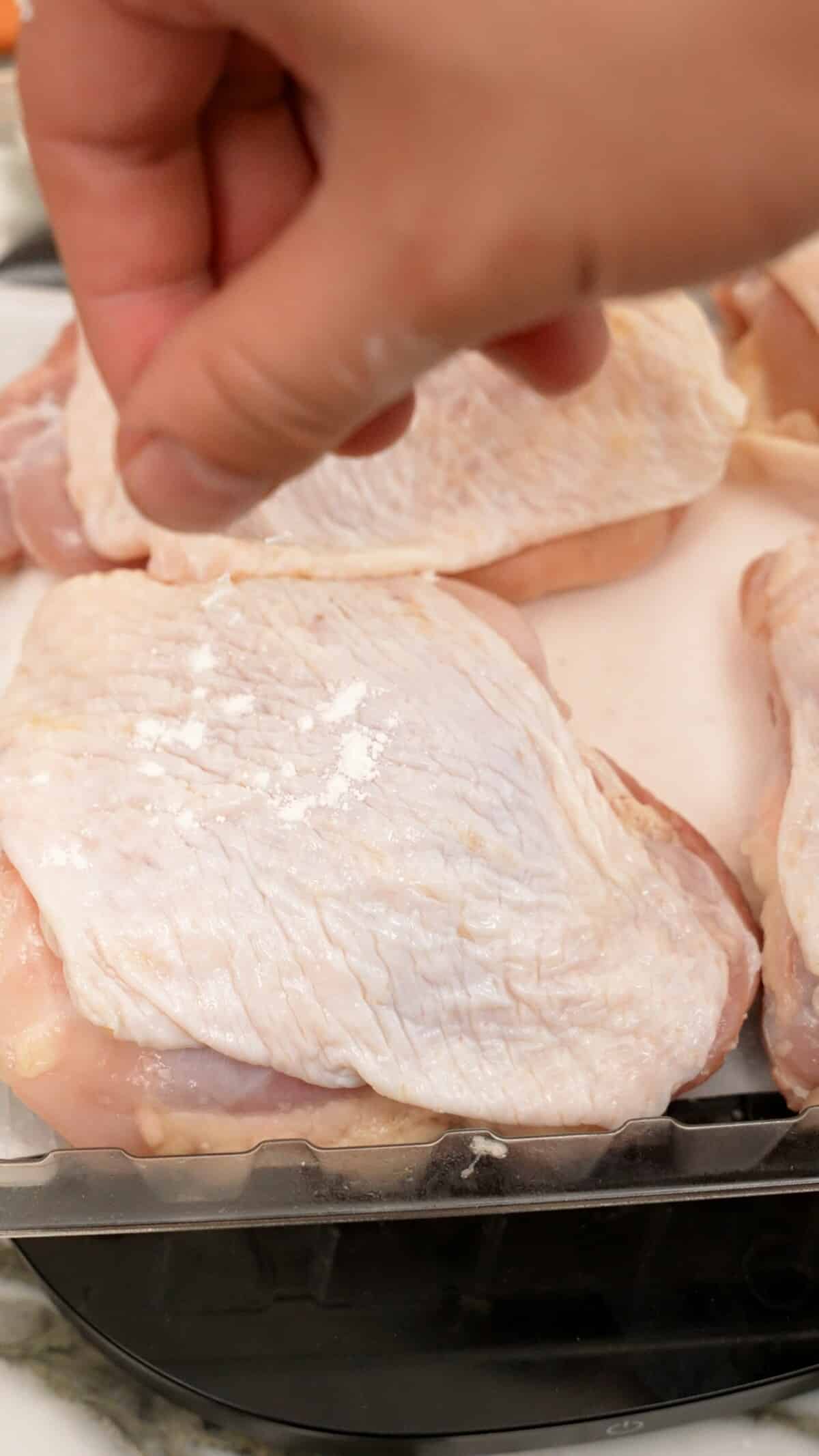 A hand sprinkling baking powder directly onto the chicken thigh skin.