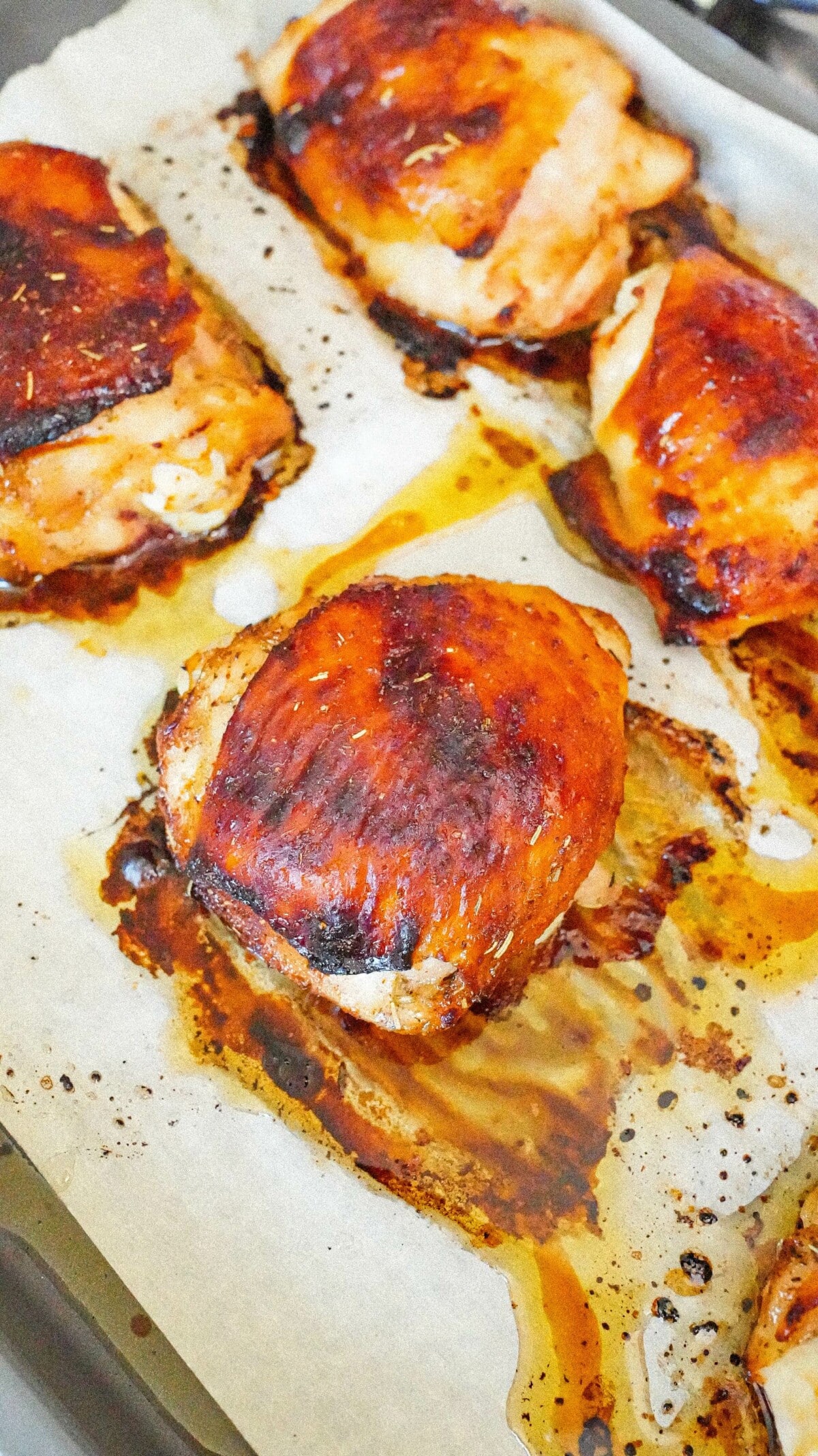 Cooked chicken thighs with a dark golden brown skin on a parchment lined baking sheet.