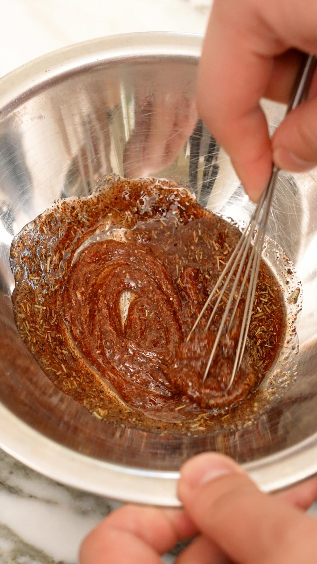 A small whisk mixing spices and seasonings in a metal bowl.