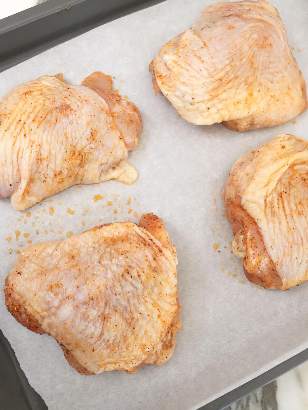 Seasoned chicken thighs on a baking sheet.